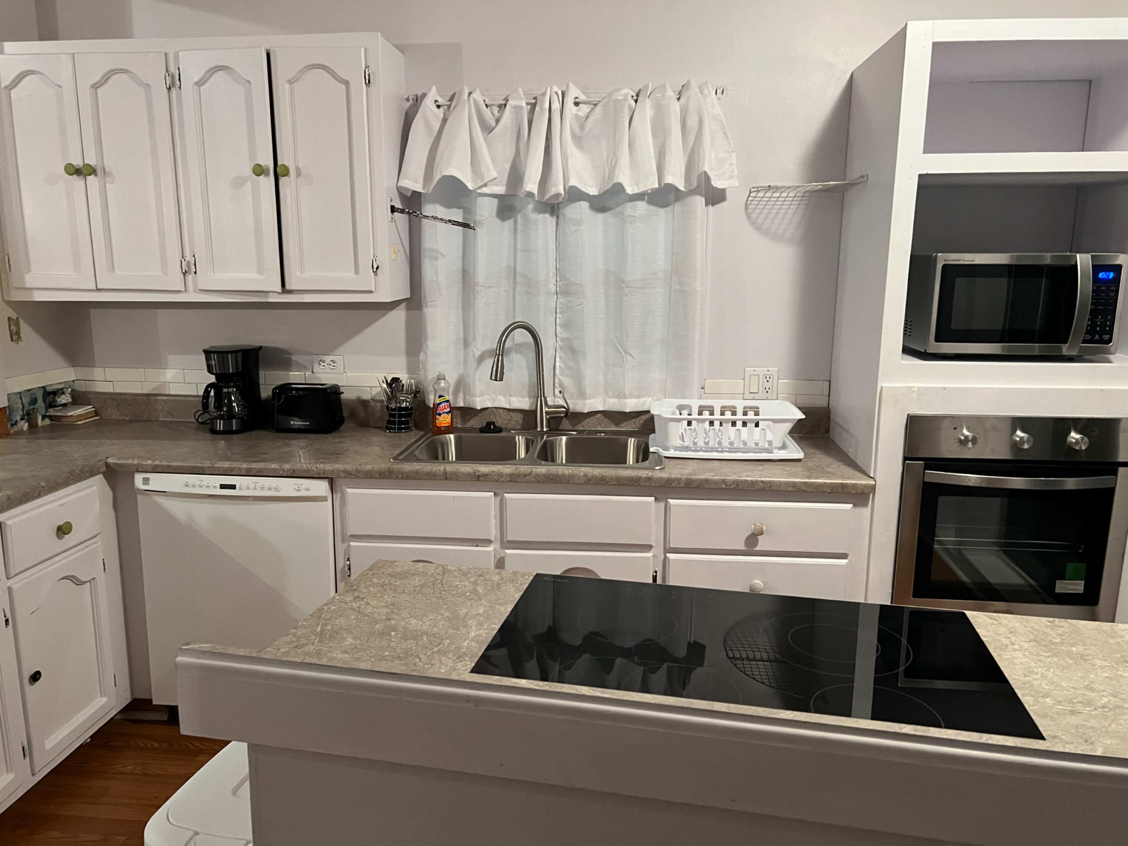 A kitchen featuring white cabinetry, a double sink, a microwave, an electric cooktop, and various appliances on the counter.