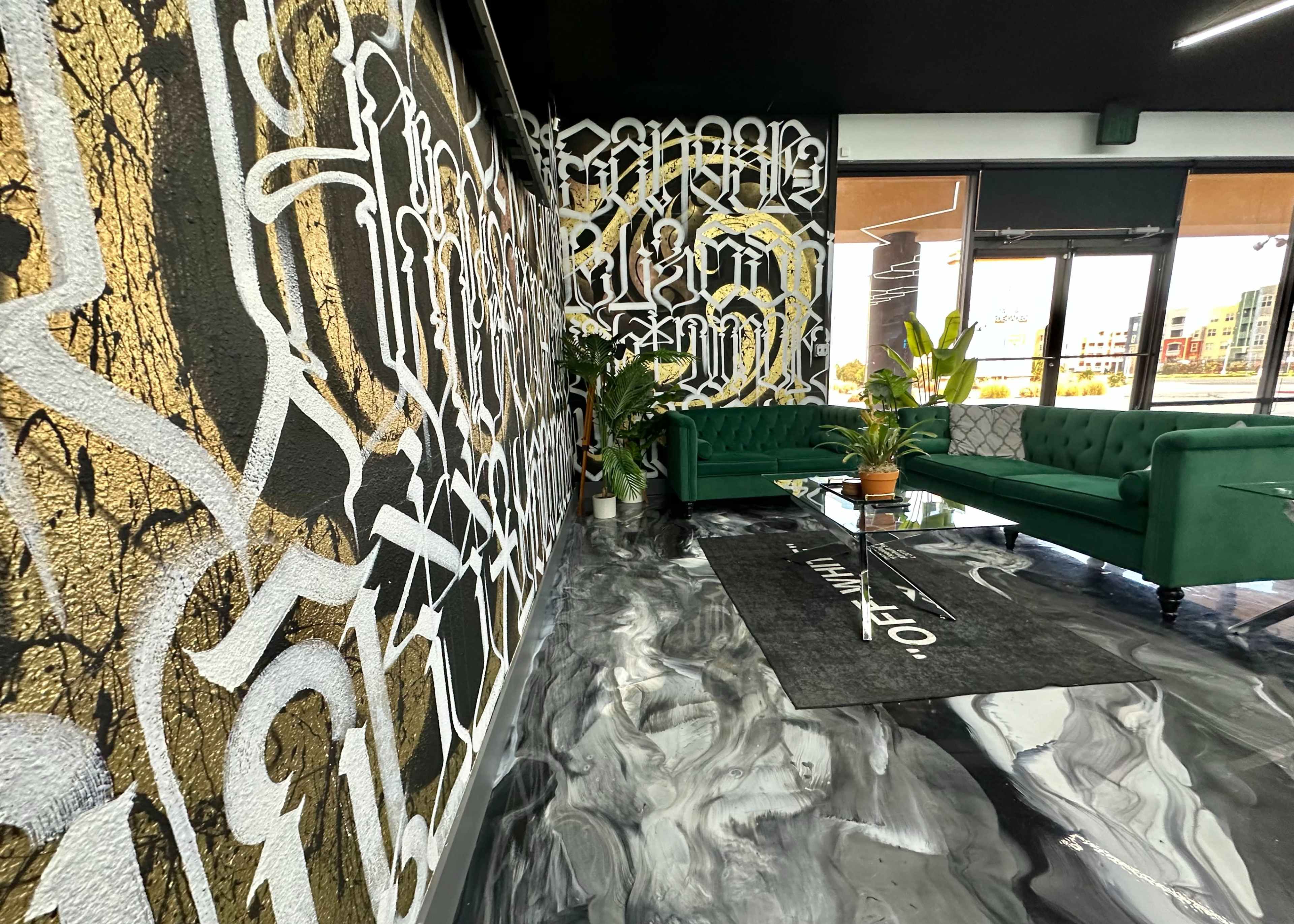 A modern lounge area featuring green velvet sofas, a patterned carpet, and abstract wall art with gold and black elements.