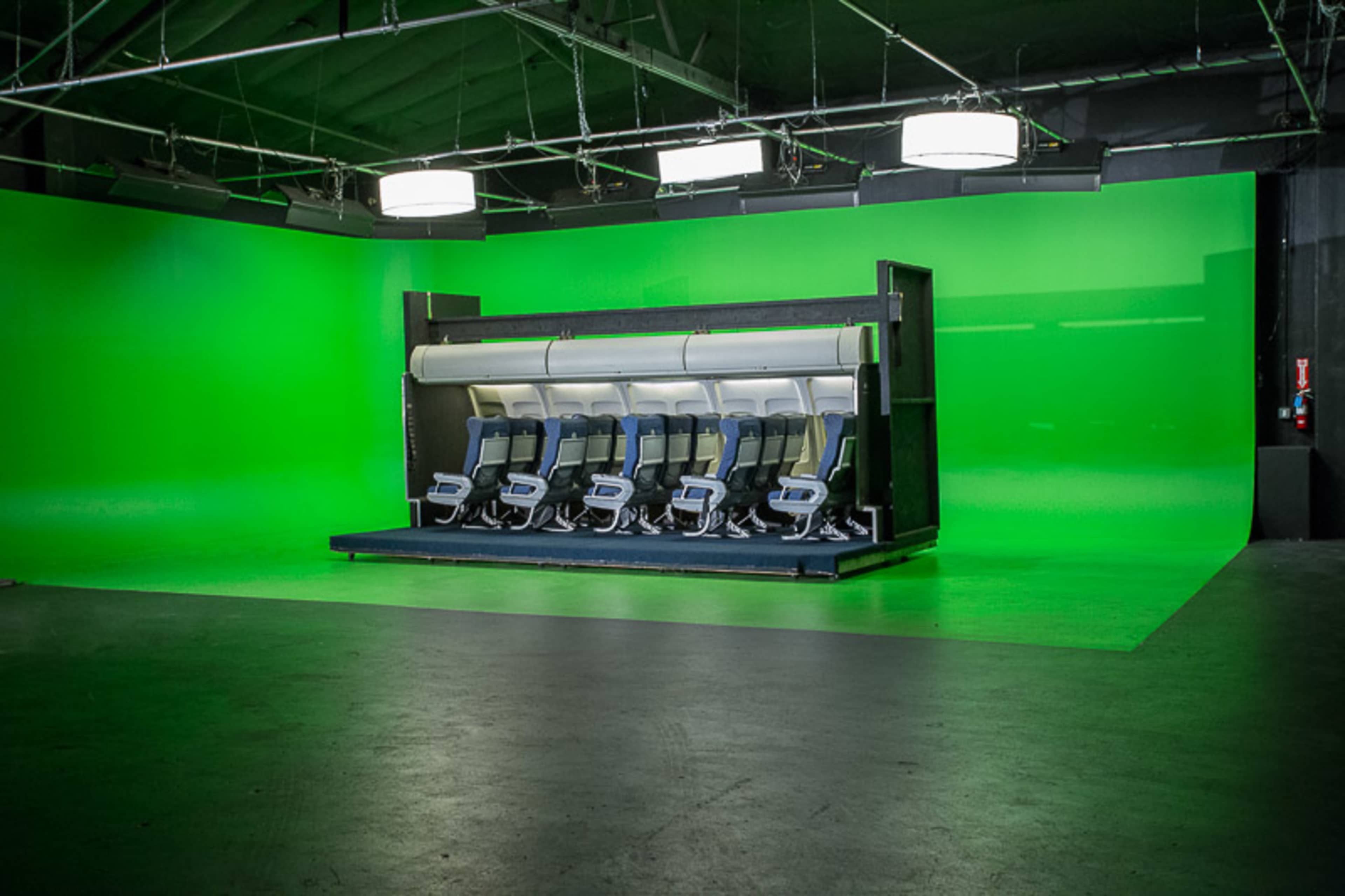 A row of six seats is lined up in front of a green screen in a studio setting.