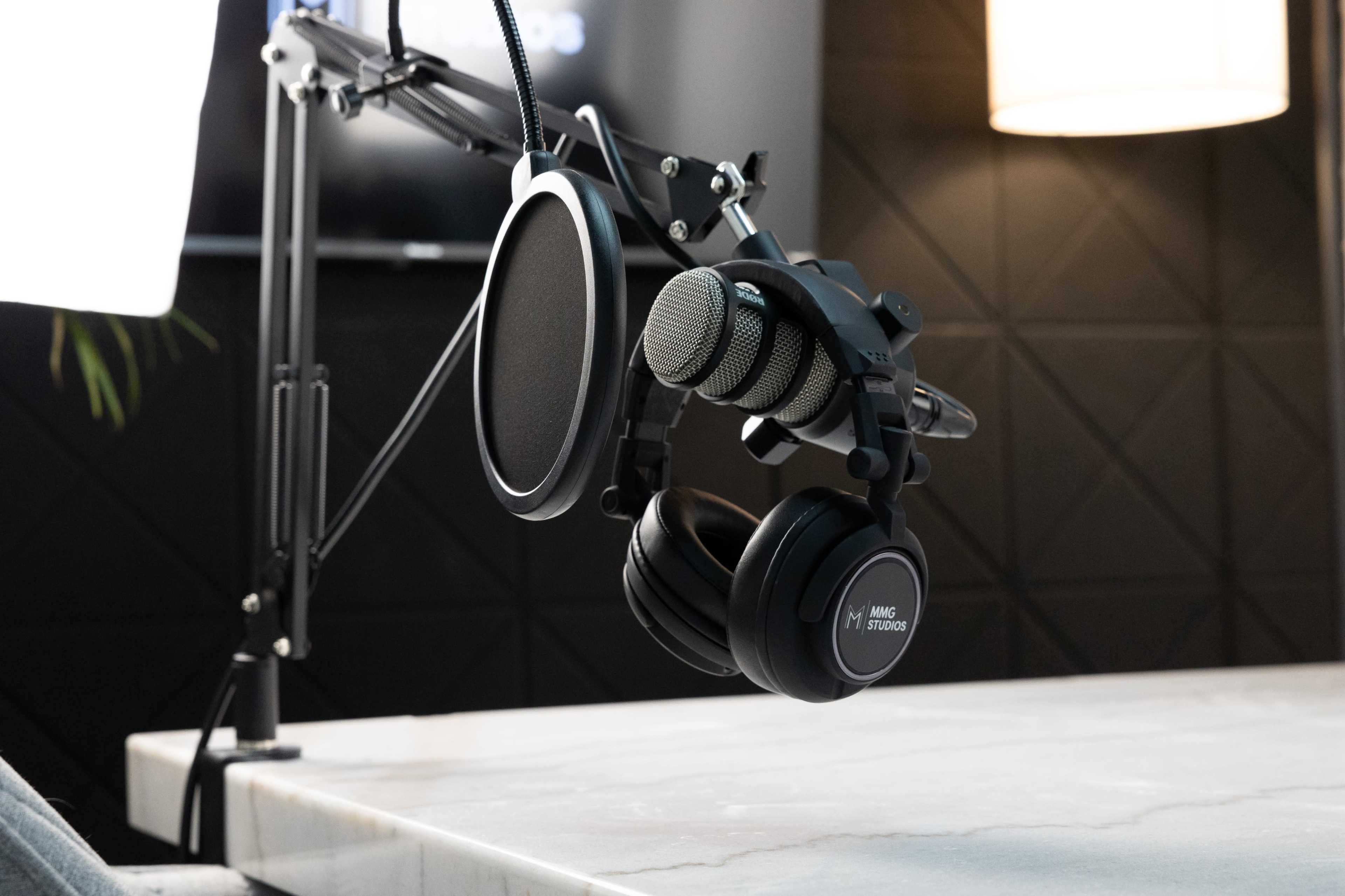 A pair of black headphones and a microphone are mounted on a sleek arm attached to a table in a modern recording studio setting.