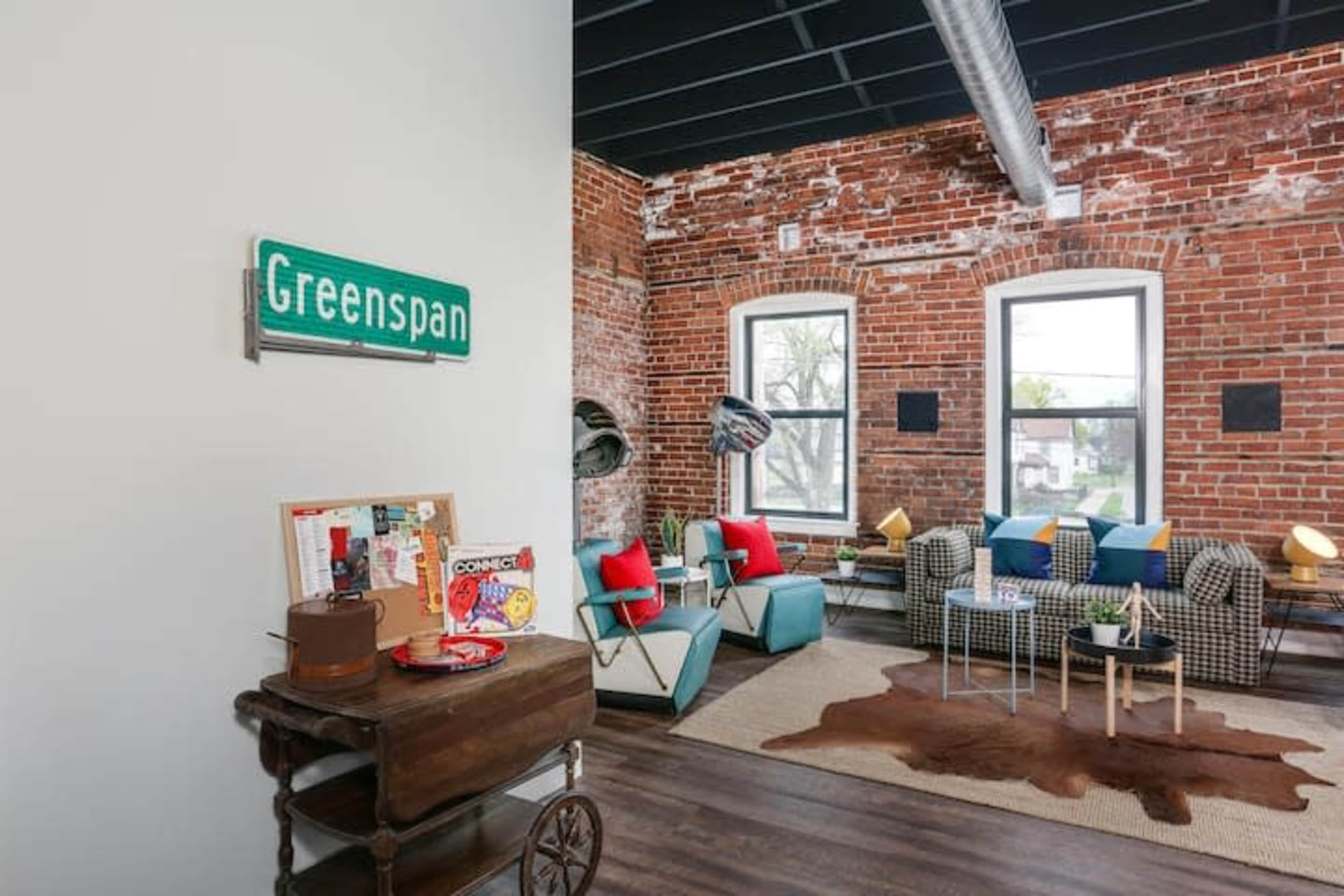 A modern living area with exposed brick walls, colorful furniture, and a decorative sign that reads "Greenspan."