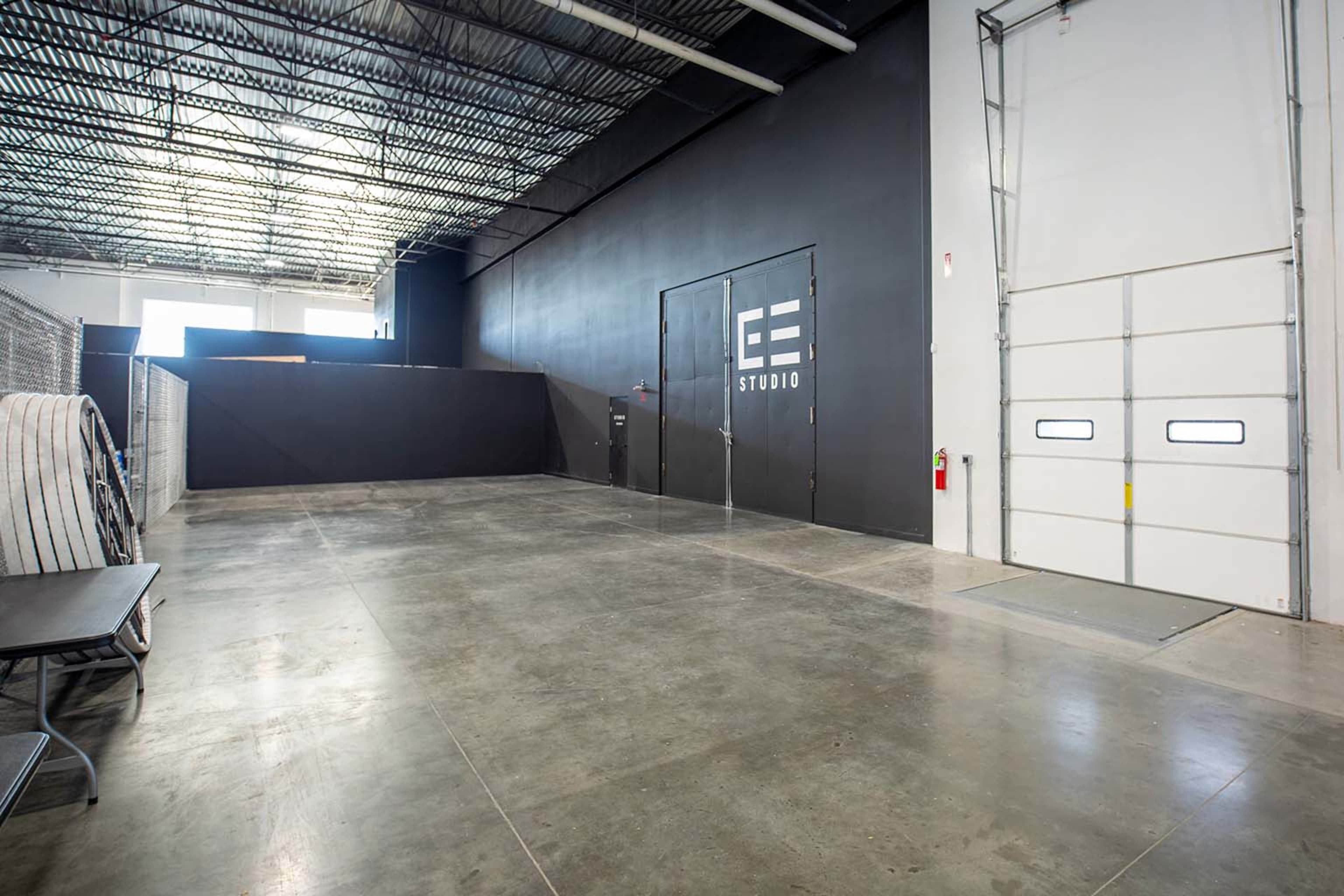 A spacious, industrial-style studio with a concrete floor and a large black wall featuring the text "EE STUDIO."