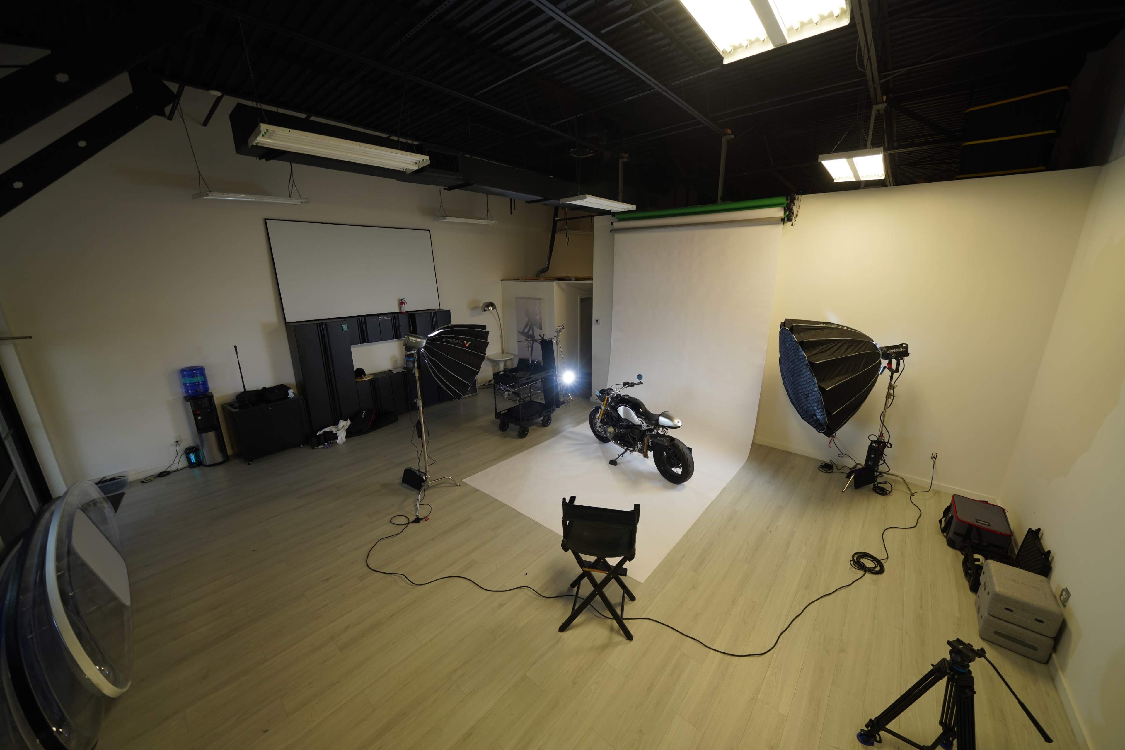 The image shows a photography studio set up with a motorcycle, two large light sources, and a backdrop.