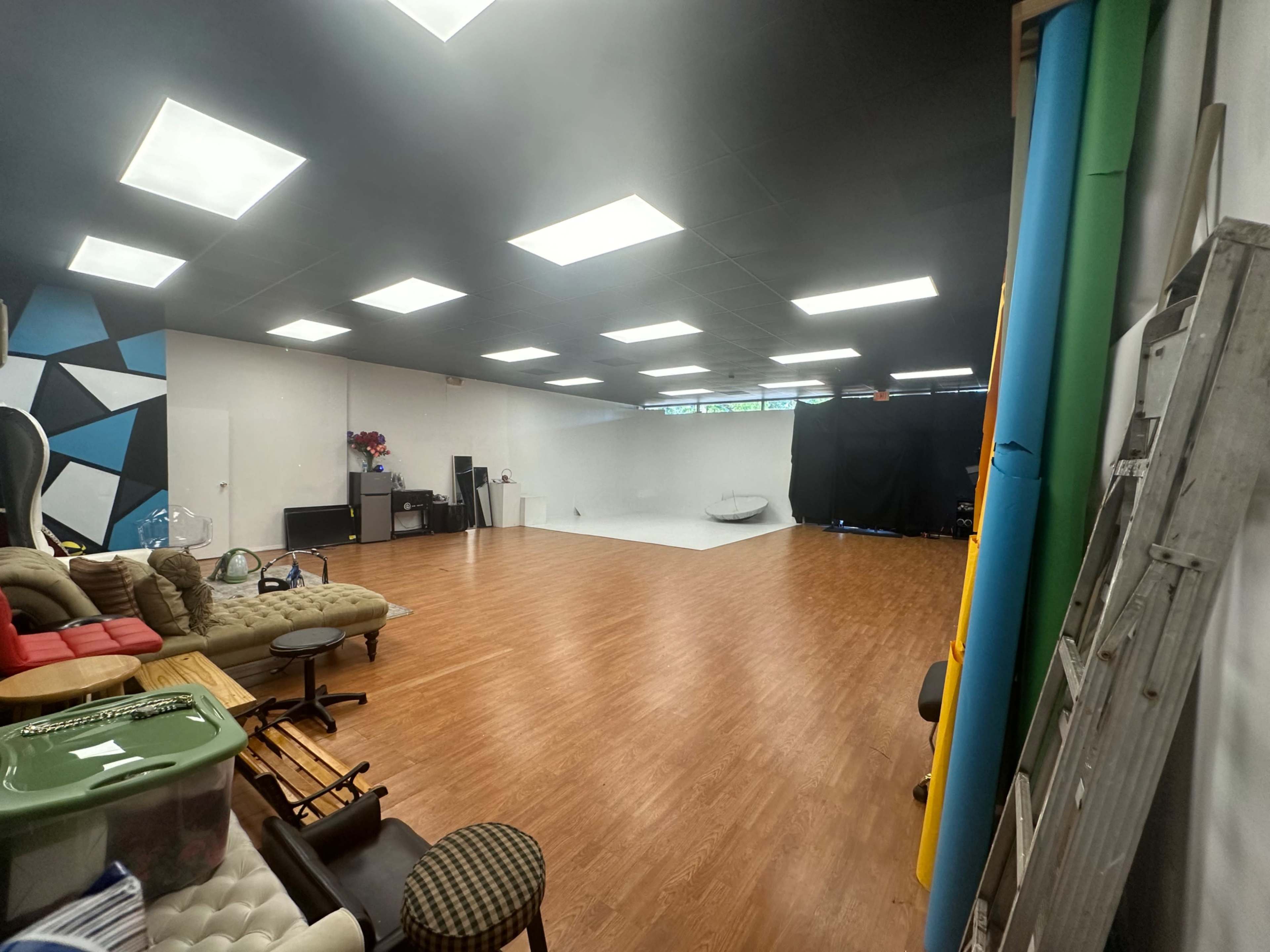A spacious studio with a wooden floor, bright lighting, and areas designated for seating and photography equipment.