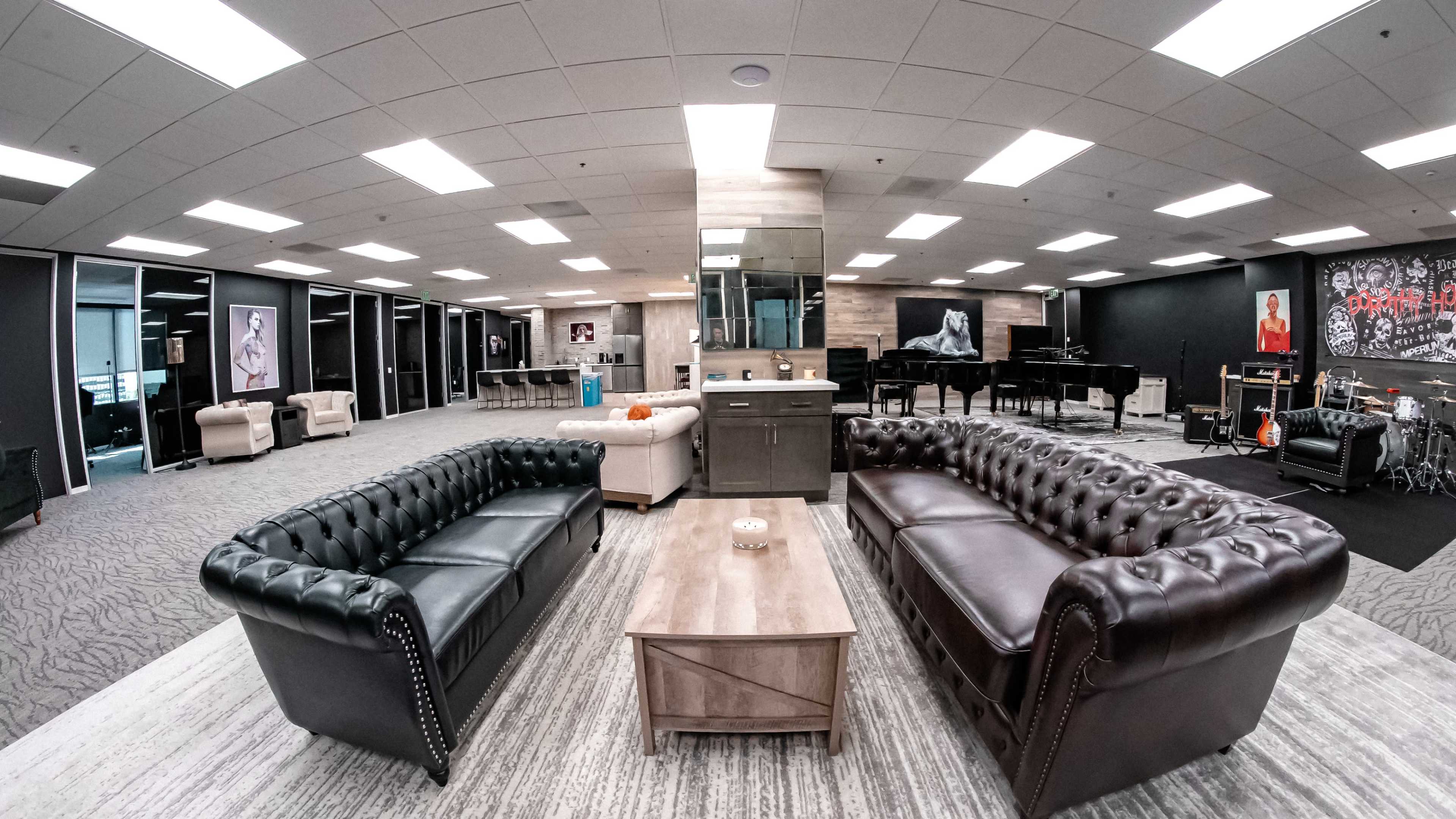 A spacious lounge area featuring two contrasting leather sofas facing a wooden coffee table, surrounded by musical instruments and artwork on the walls.