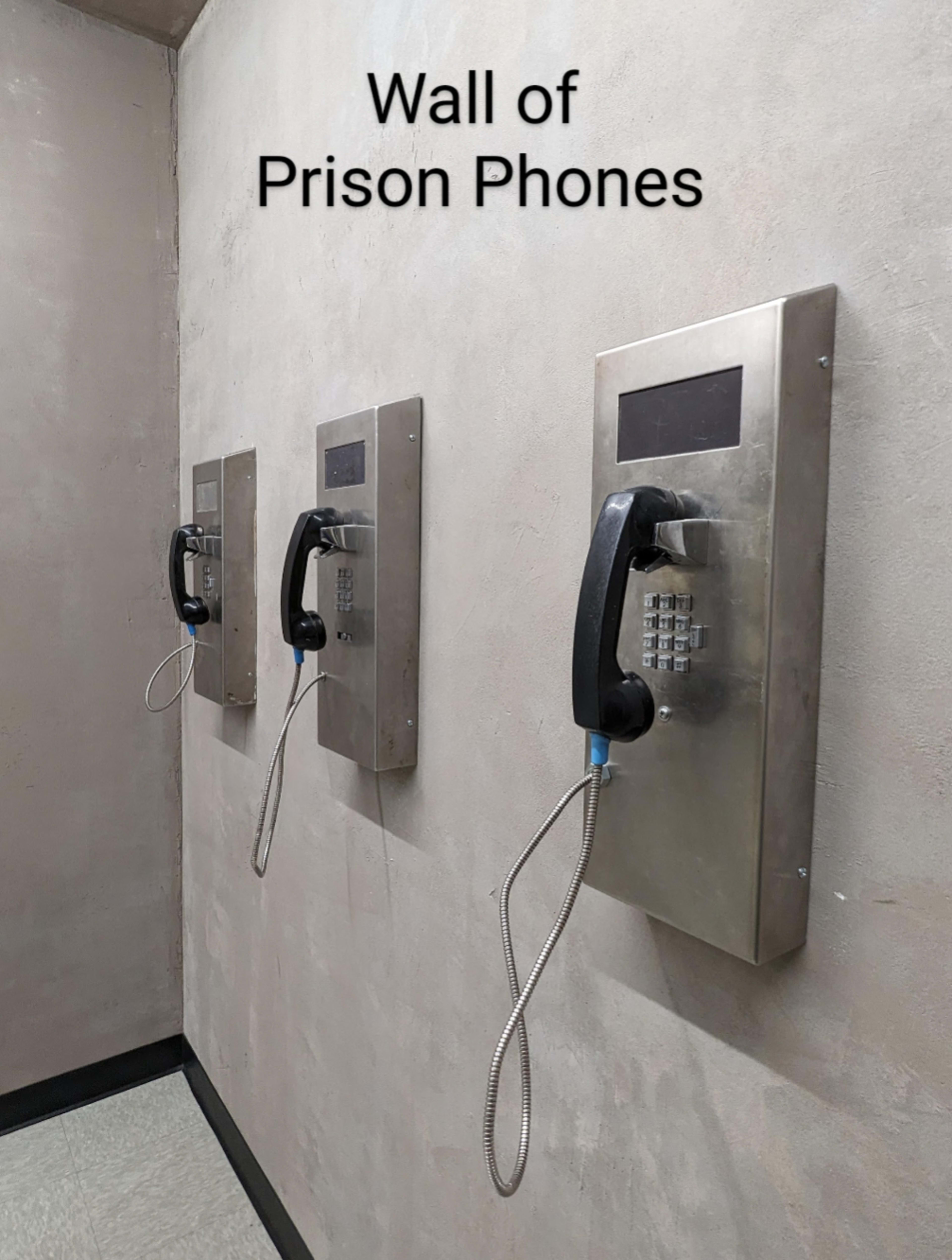 The image shows a wall with three prison phones mounted on metal plates.