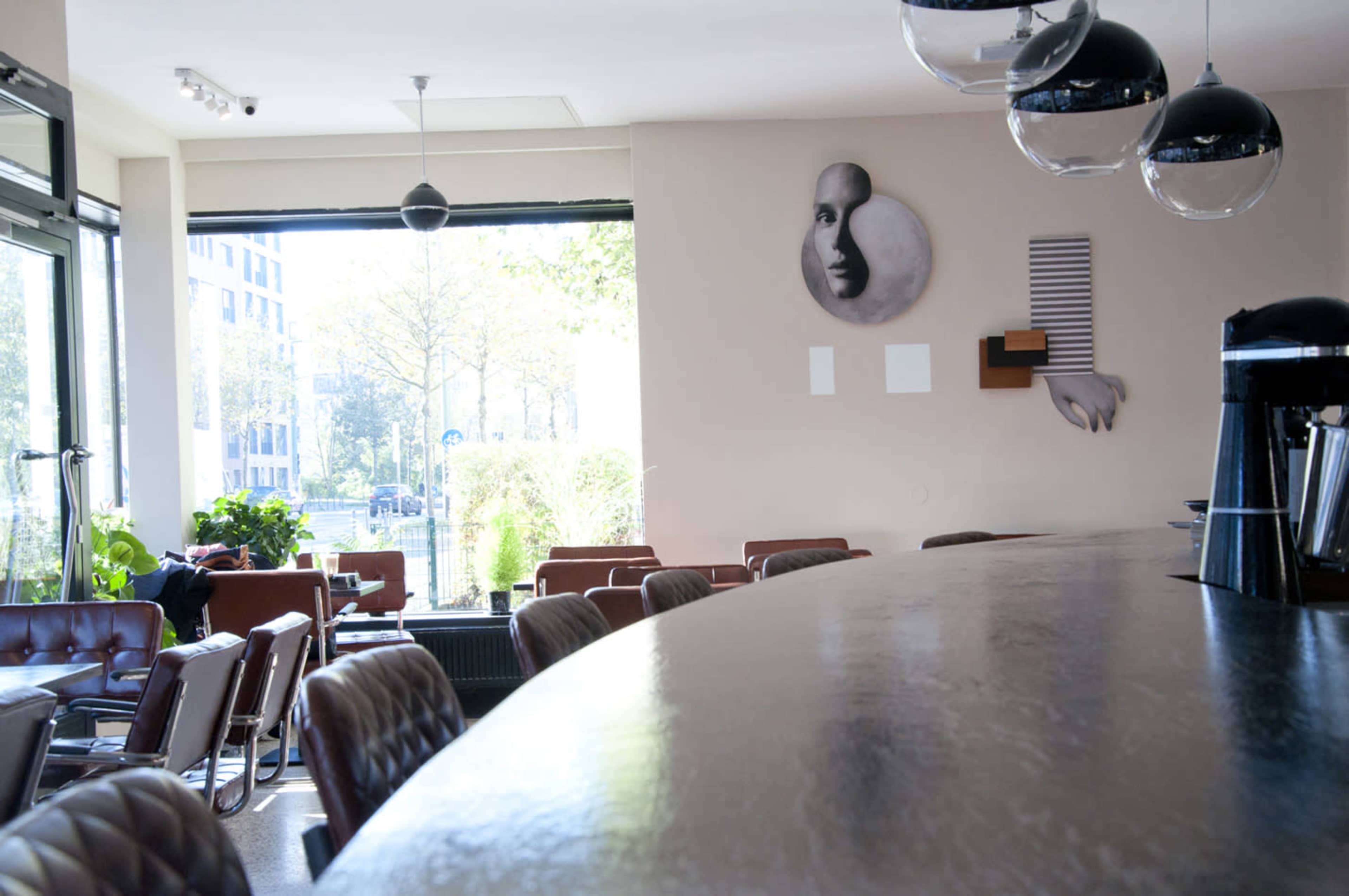 The image shows a modern café interior with a long bar counter, leather seating, and large windows letting in natural light.