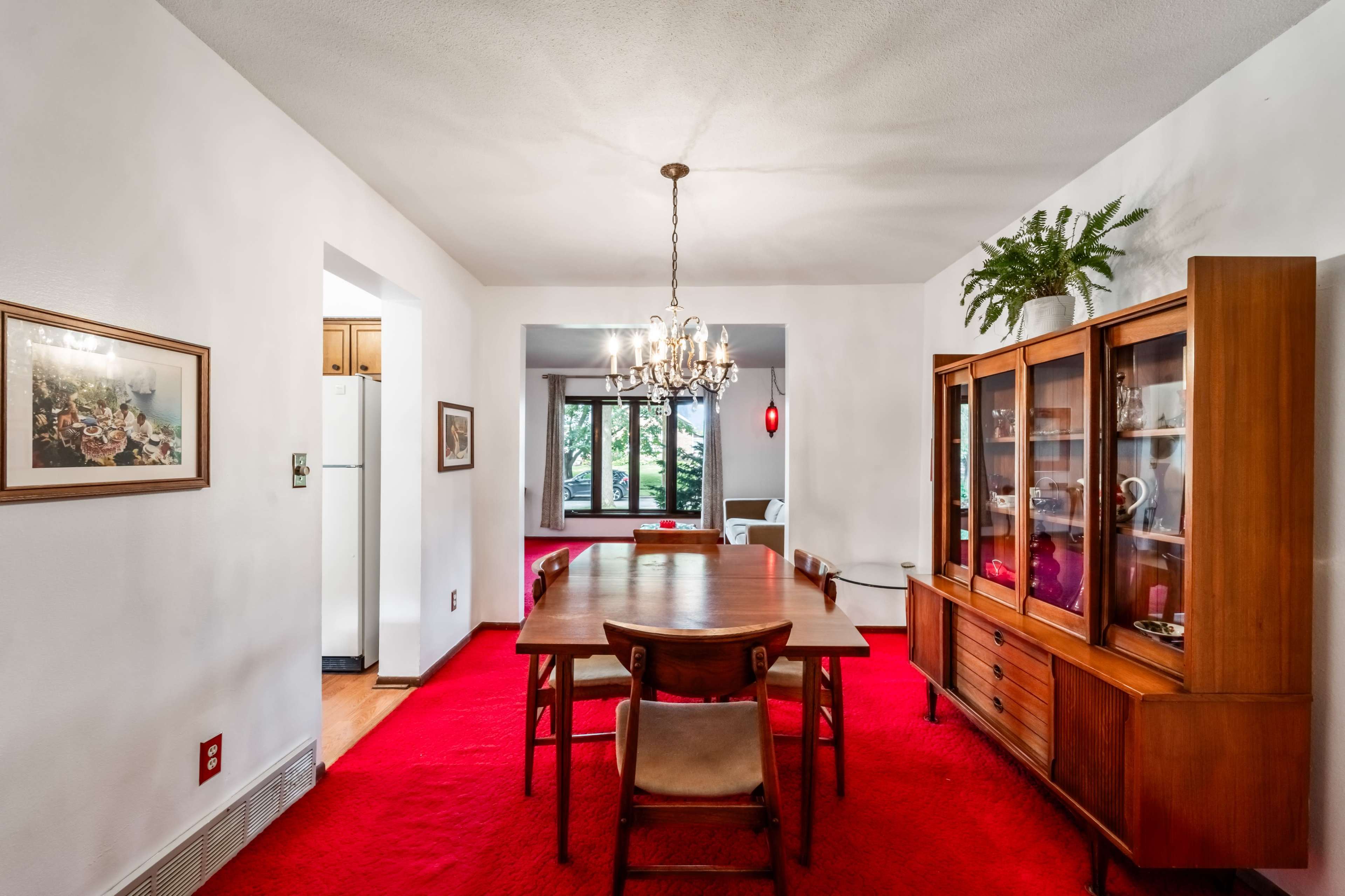 A dining room features a wooden table surrounded by chairs, a chandelier overhead, and a china cabinet against the wall.