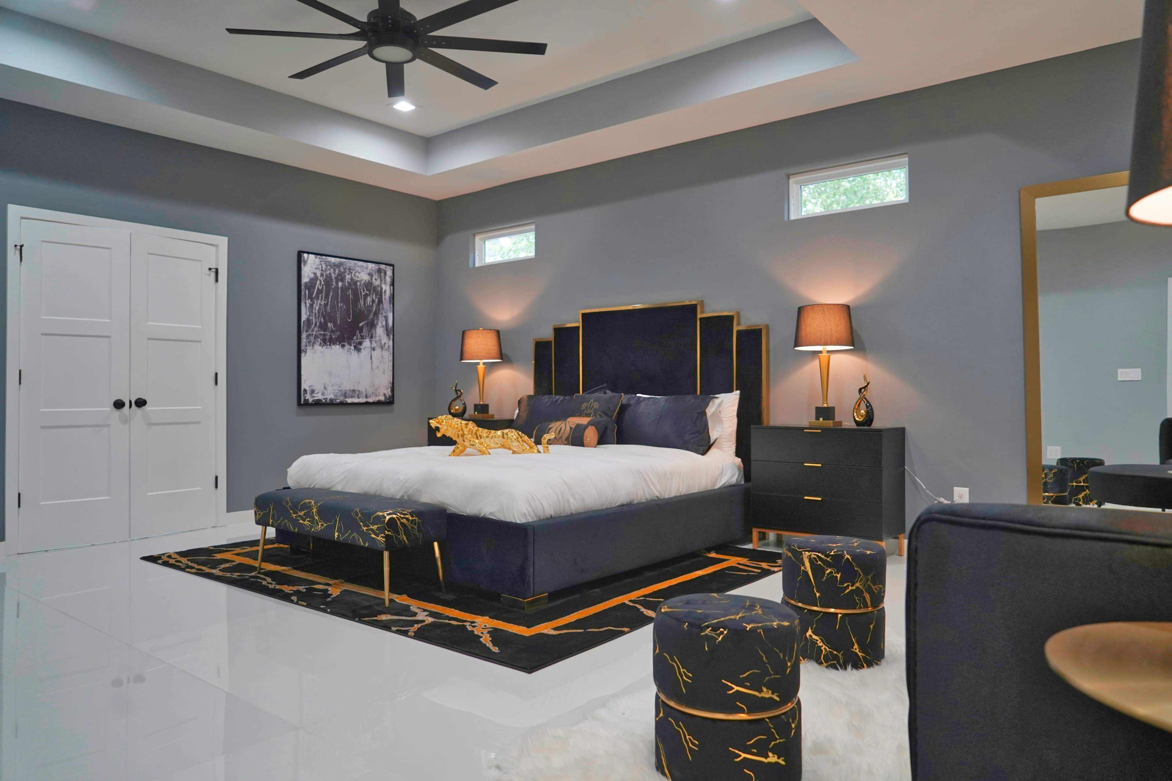 A modern bedroom with a large bed, two bedside lamps, a decorative rug, and a stylish dresser against gray walls.