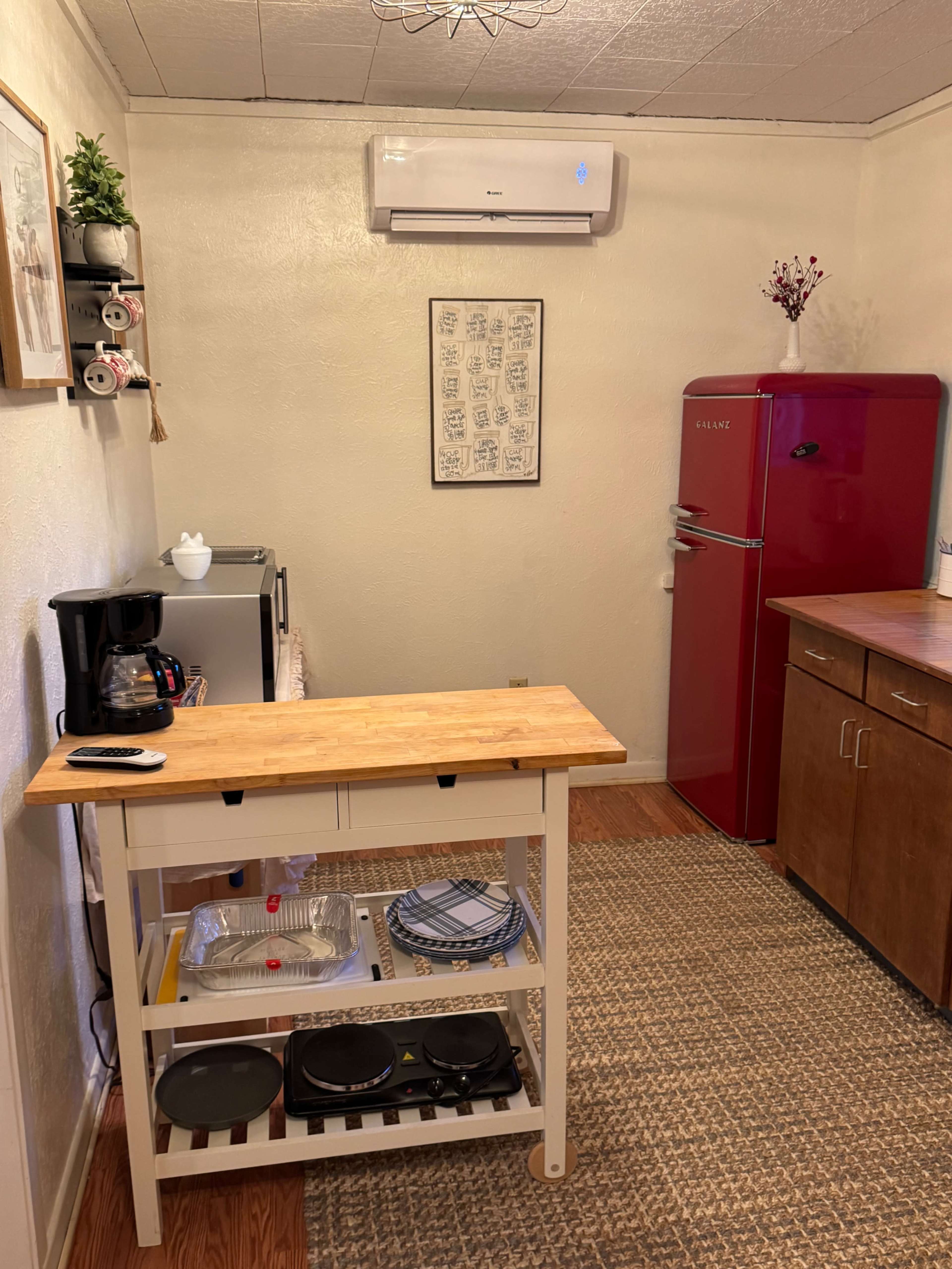 The image shows a small kitchen featuring a wooden island, a red refrigerator, and various kitchen appliances along with a rug on the floor.