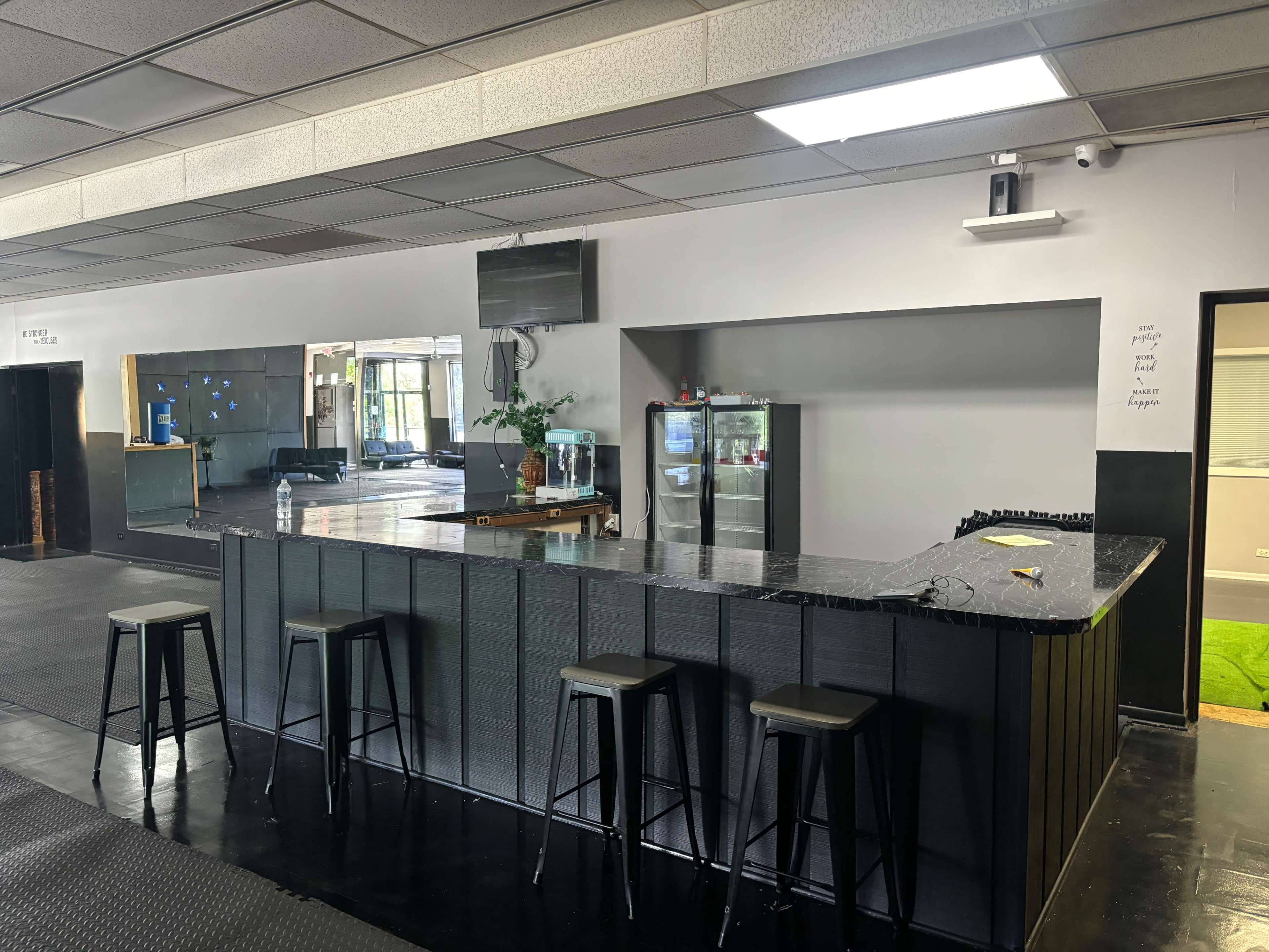 A sleek, modern bar area features a dark countertop and several high stools, with a refrigerator and a television mounted on the wall behind it.