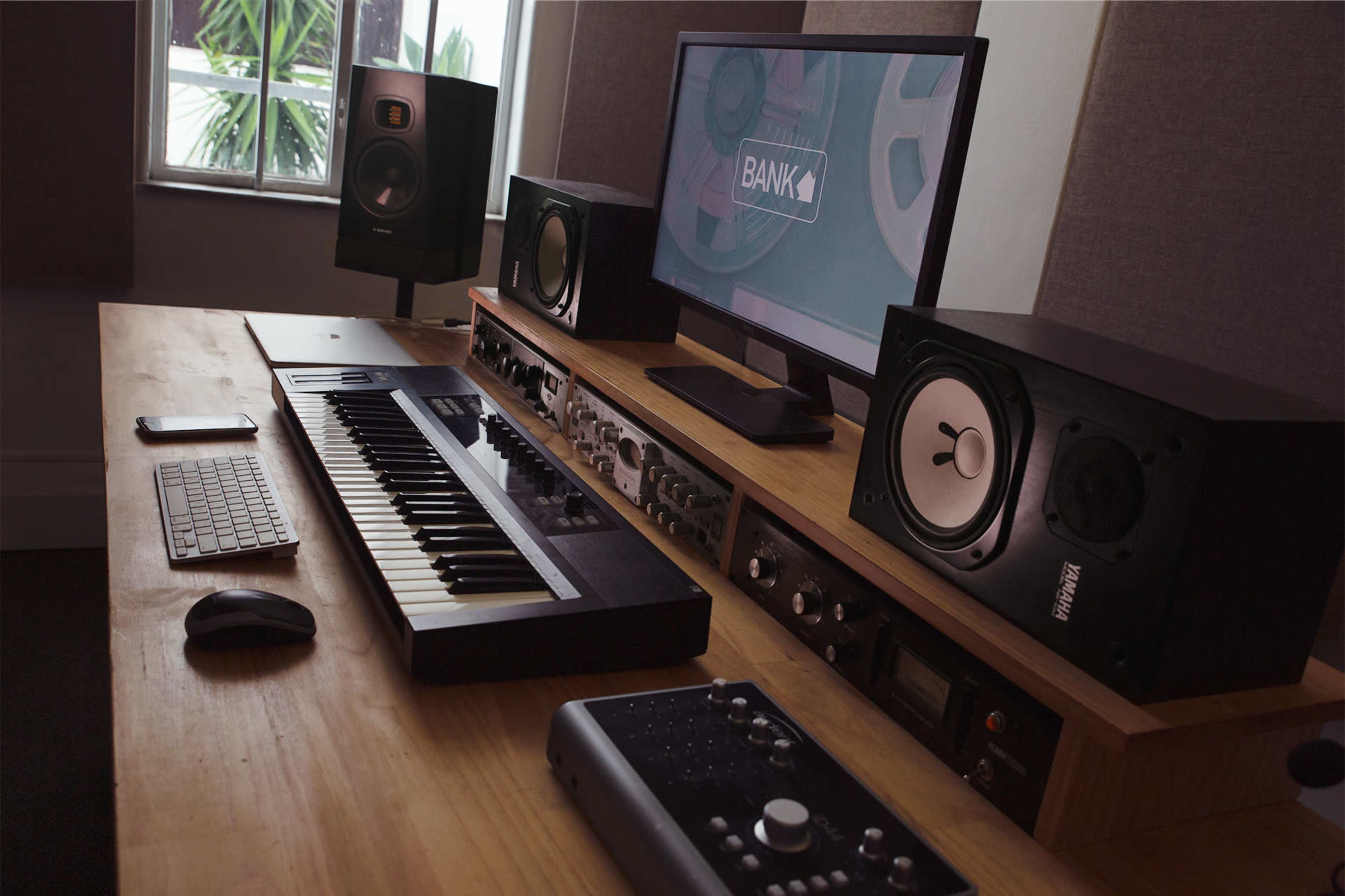 A modern music production setup featuring a keyboard, audio interface, computer, and studio monitors on a wooden desk.