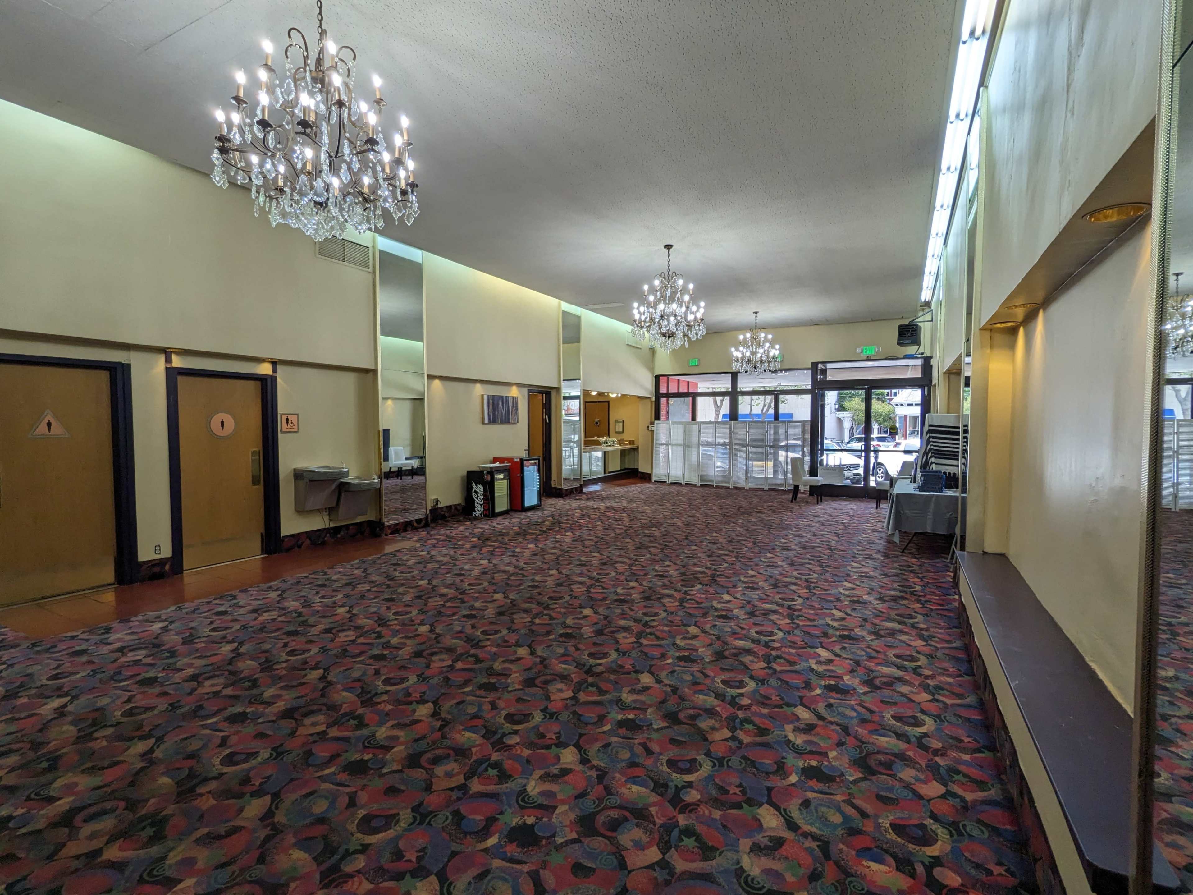 A spacious lobby with patterned carpet, chandeliers overhead, and several doors leading to other areas.