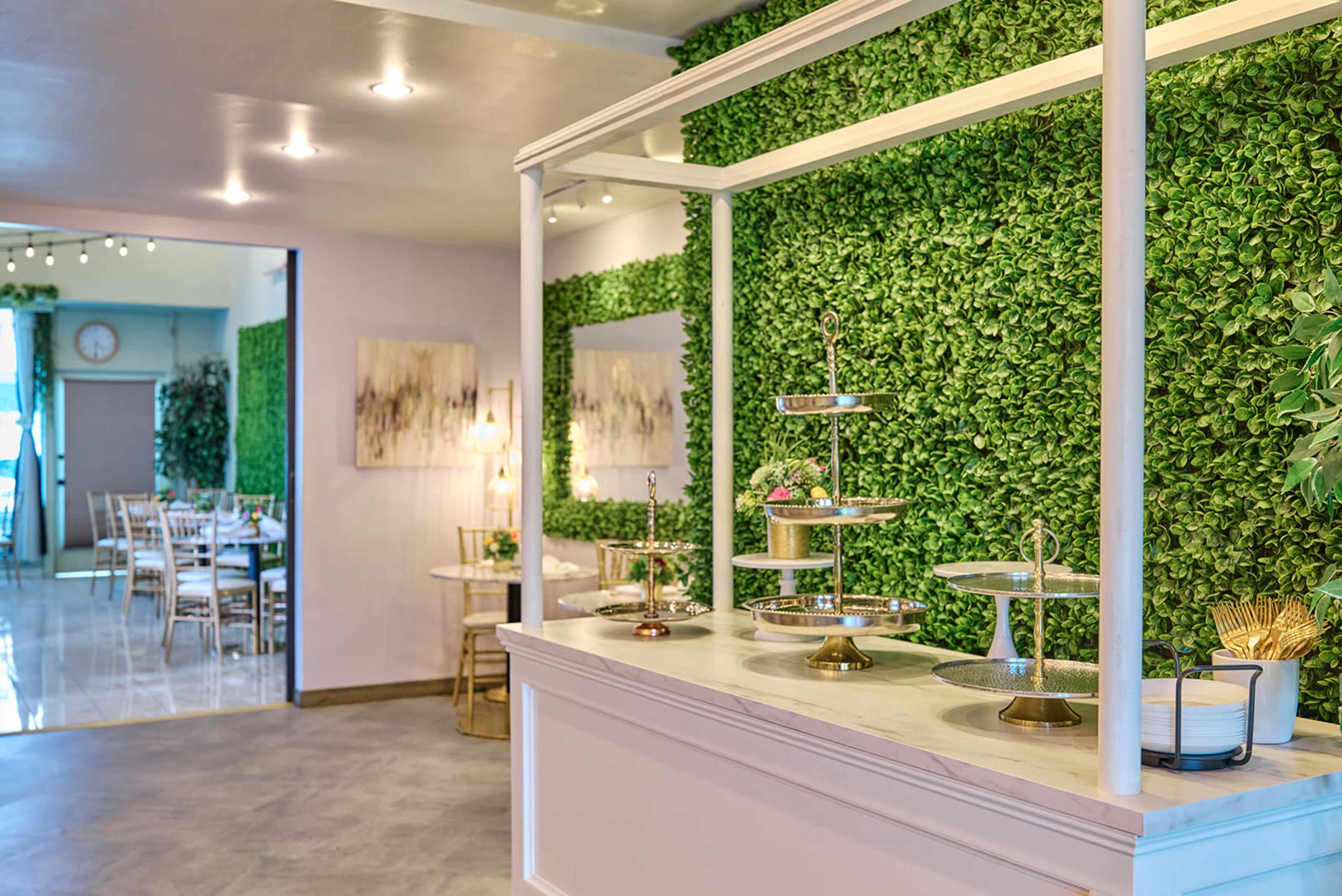 The image shows a modern interior of a restaurant featuring a decorative green wall and a display stand with multiple tiers for serving food.