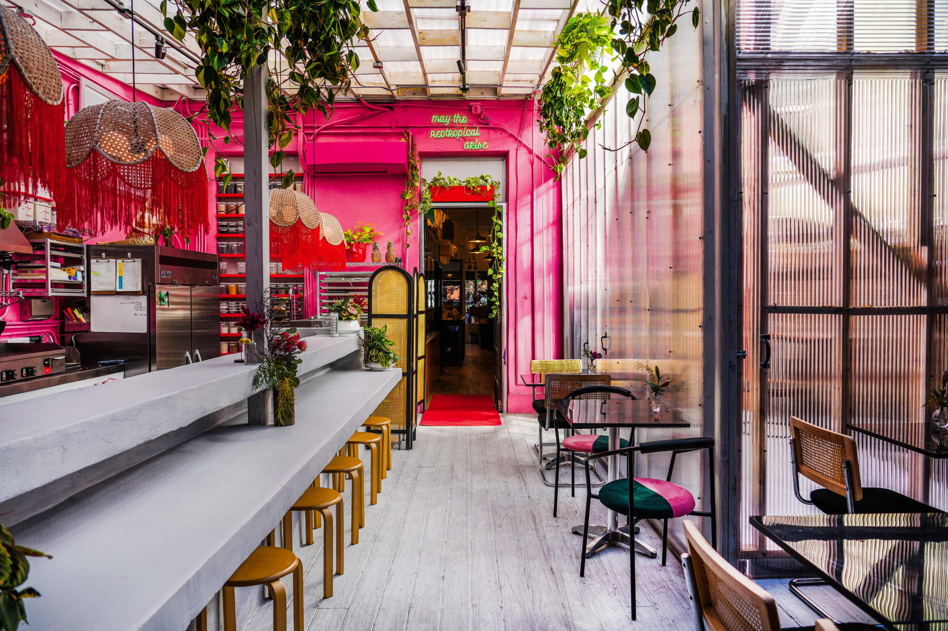 The image shows a brightly colored restaurant interior with pink decor, a long white counter, and various seating arrangements.