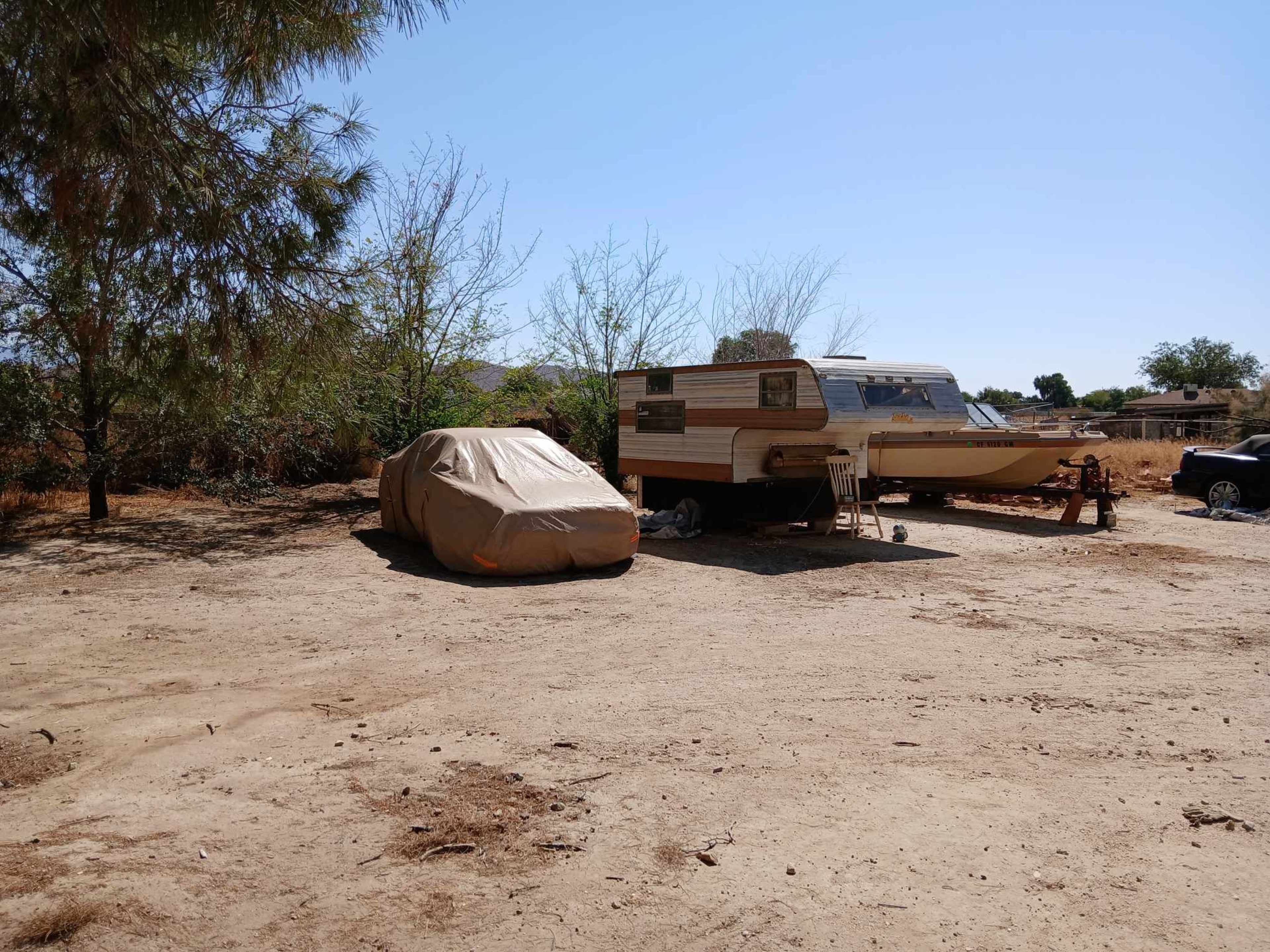 A covered vehicle sits next to a parked trailer in a dry, sparsely vegetated area.