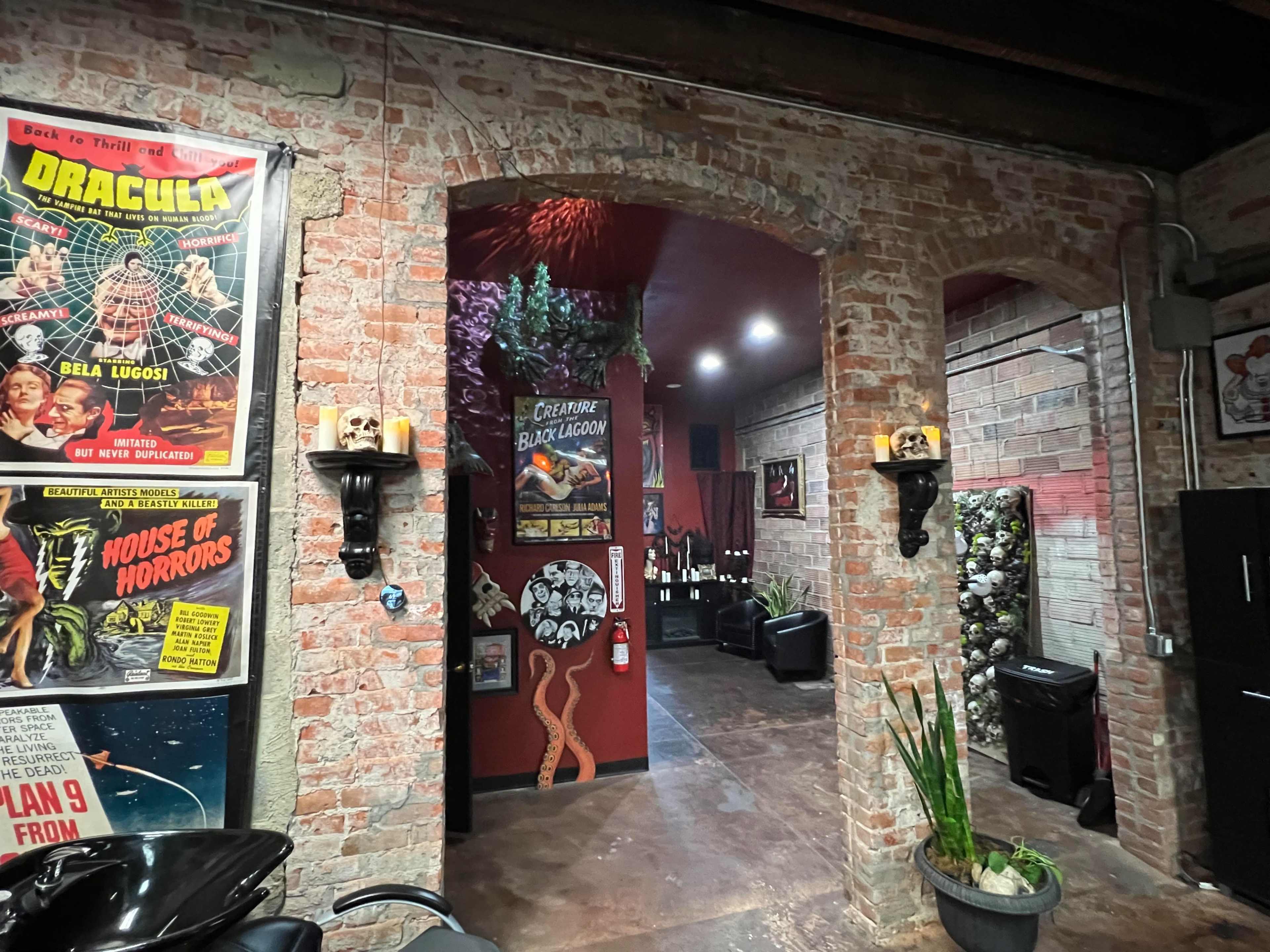 A brick-walled corridor leading to a themed room decorated with horror movie posters and dark furnishings.