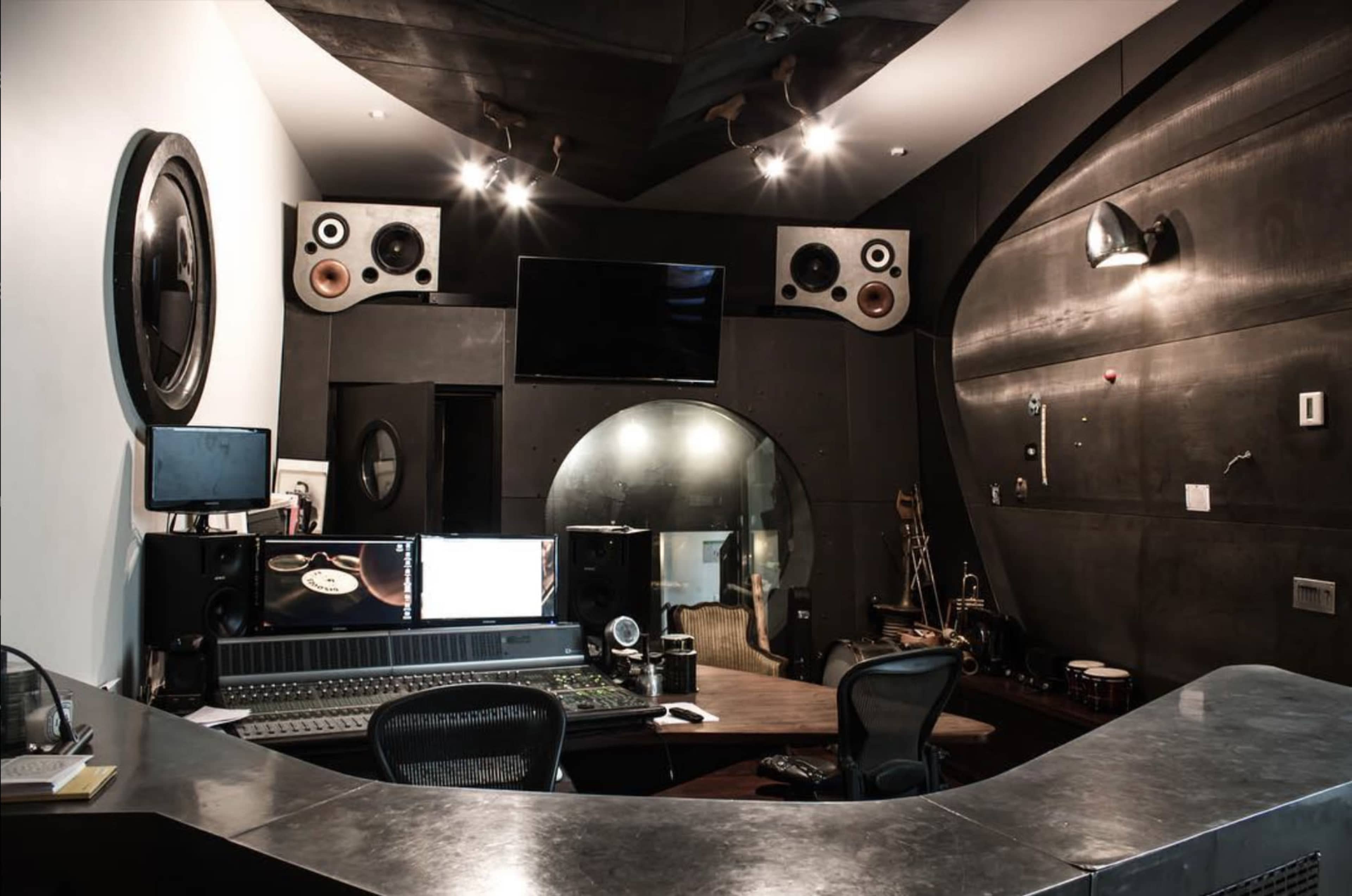 A modern recording studio with sound equipment, large speakers, and a control desk in a dimly lit space.