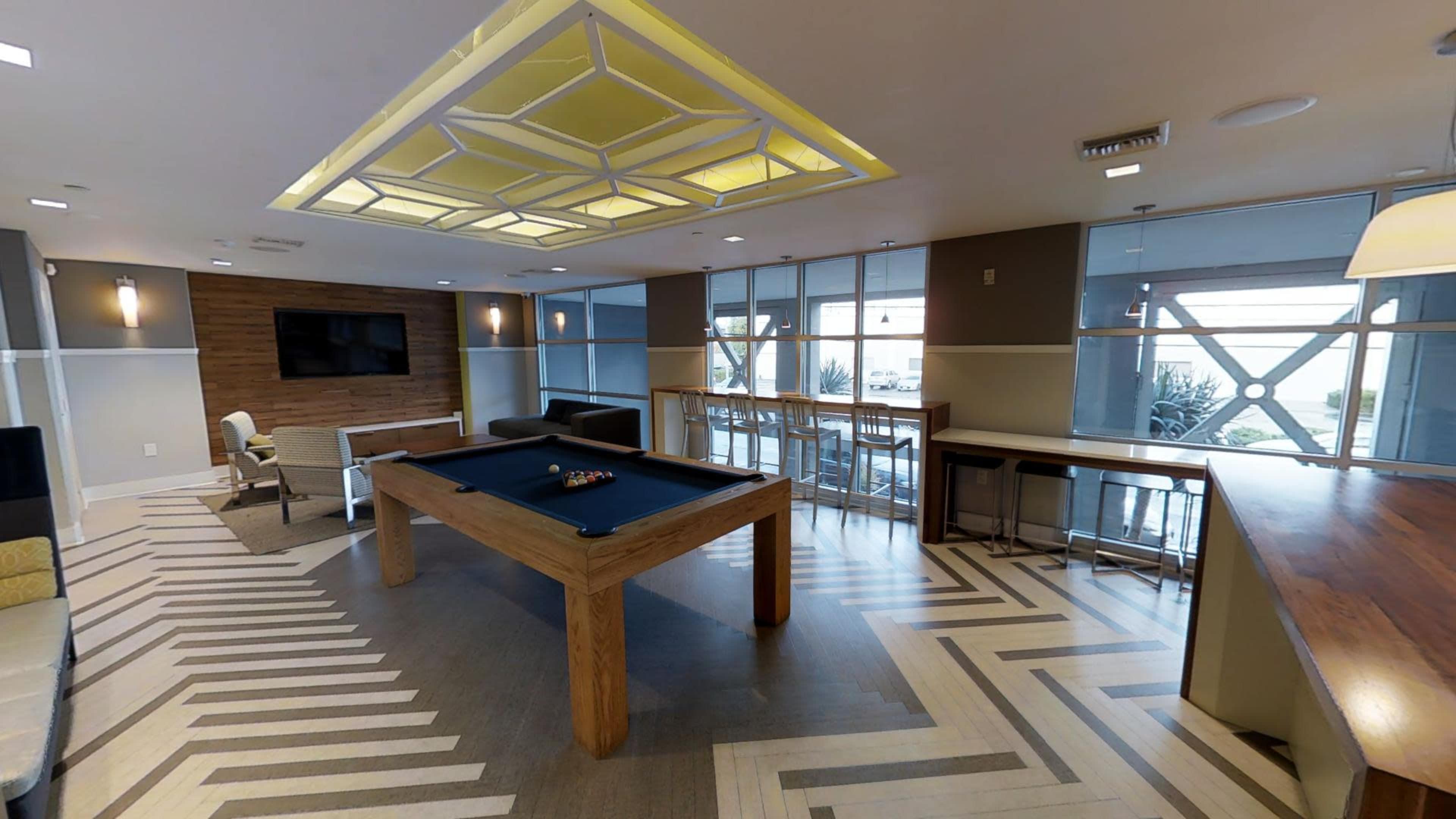 A lounge area featuring a pool table, seating arrangements, large windows, and a bar counter.