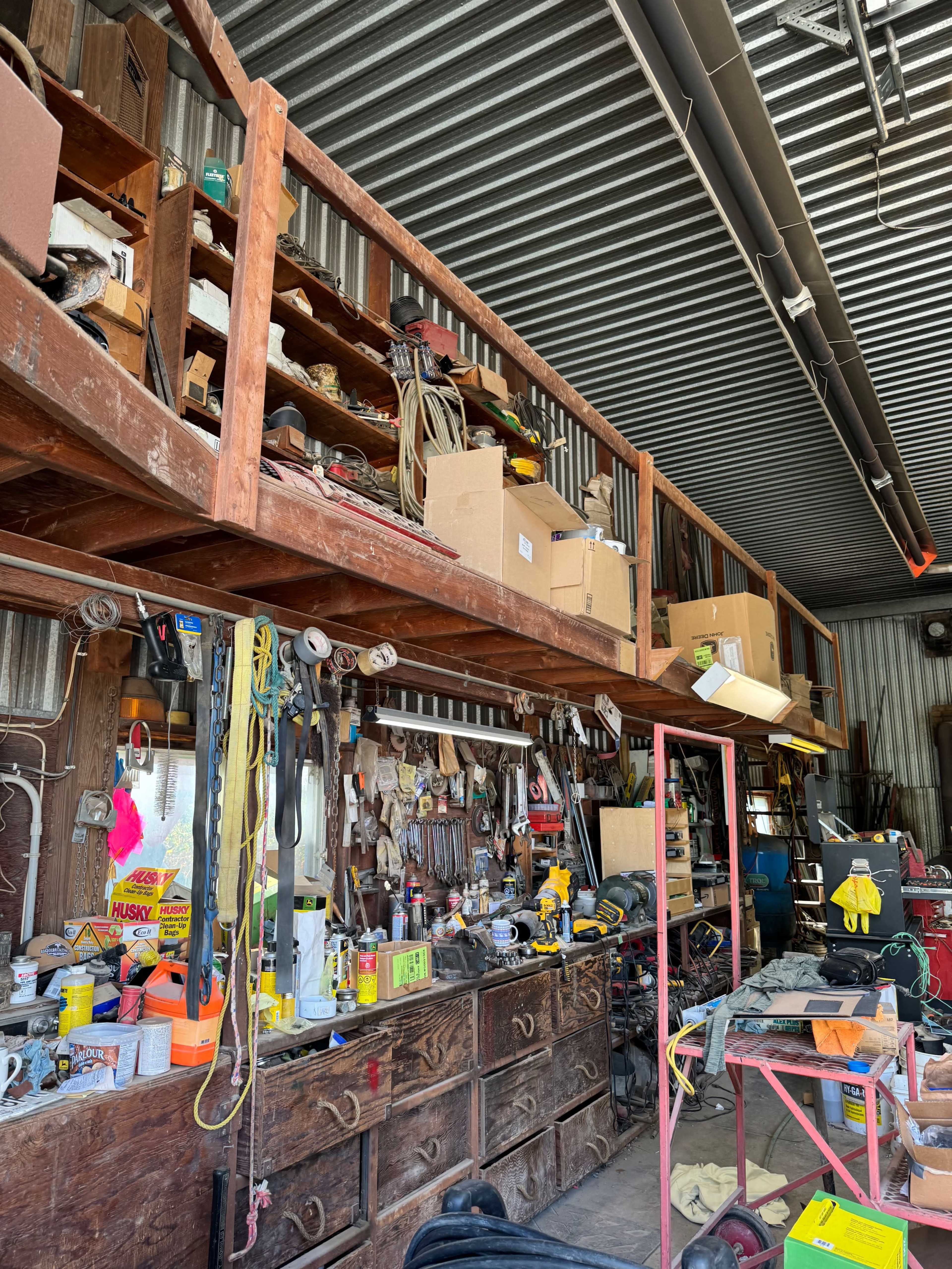 The image shows a cluttered workshop with shelves filled with boxes and tools, along with various equipment and materials on the ground.