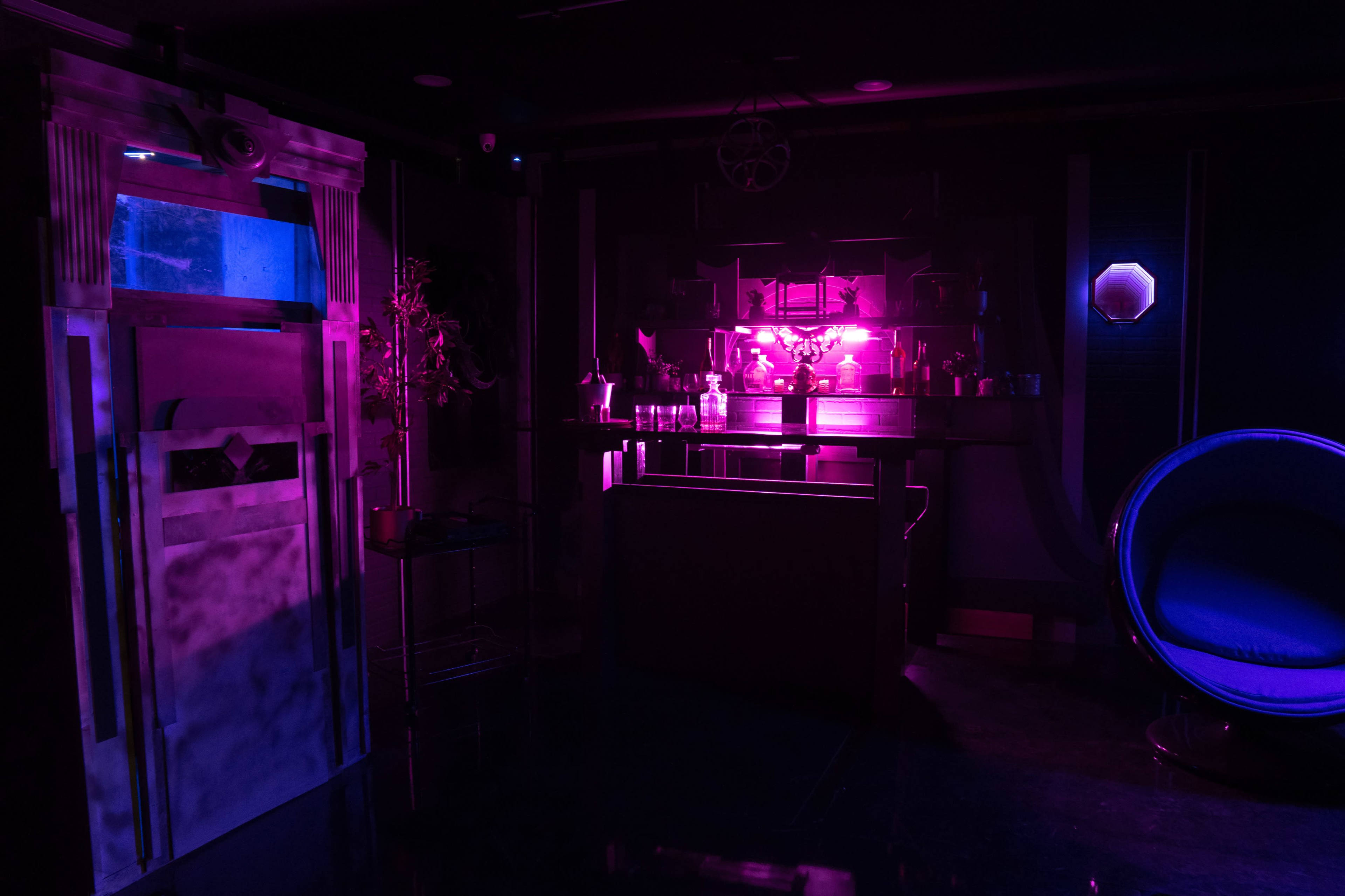 A dimly lit room featuring a bar, a circular blue chair, and a door illuminated by purple and blue light.