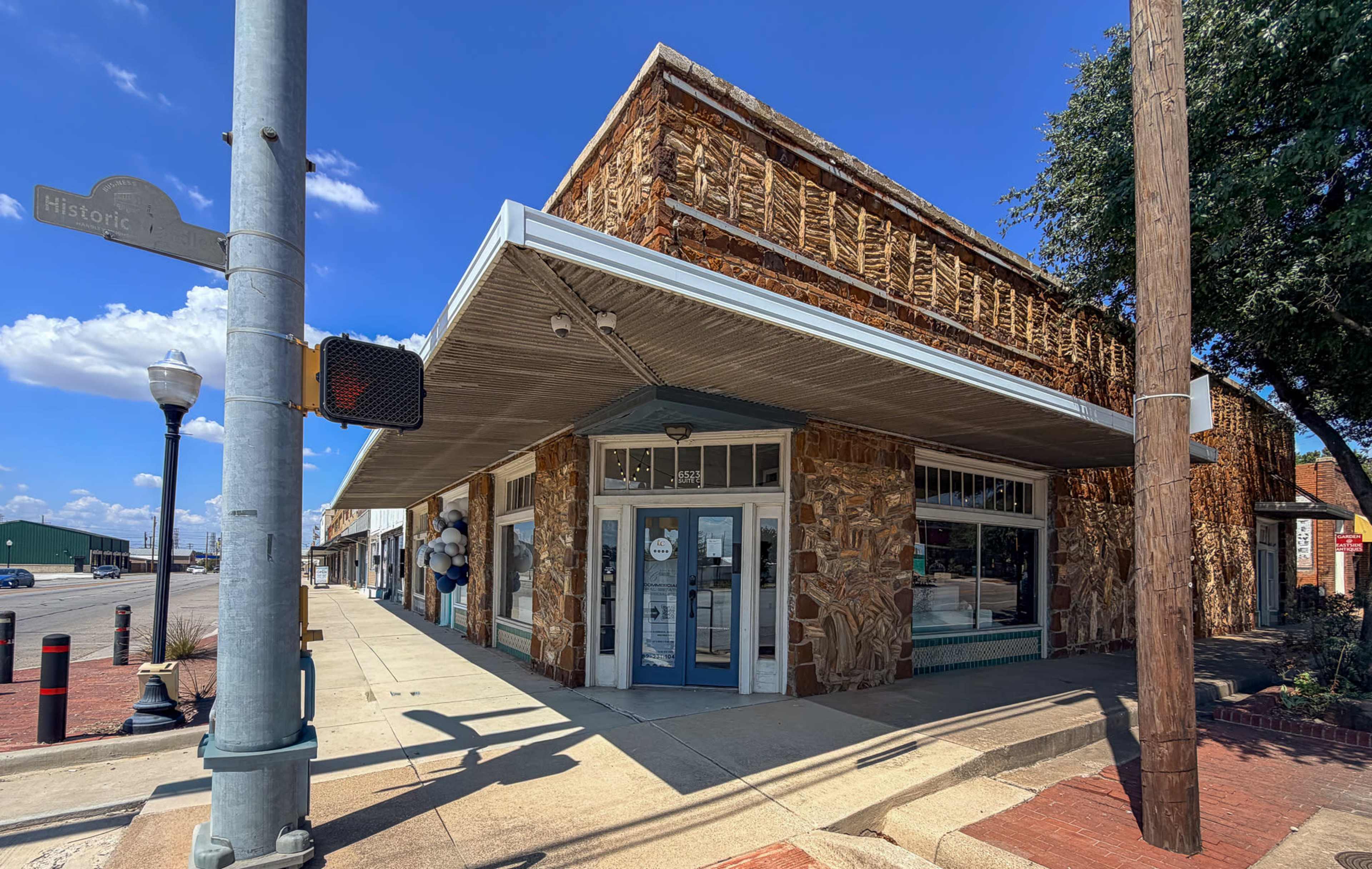 A historic stone building with a modern awning and large windows is situated at the intersection of a street with a traffic signal and a wooden utility pole.