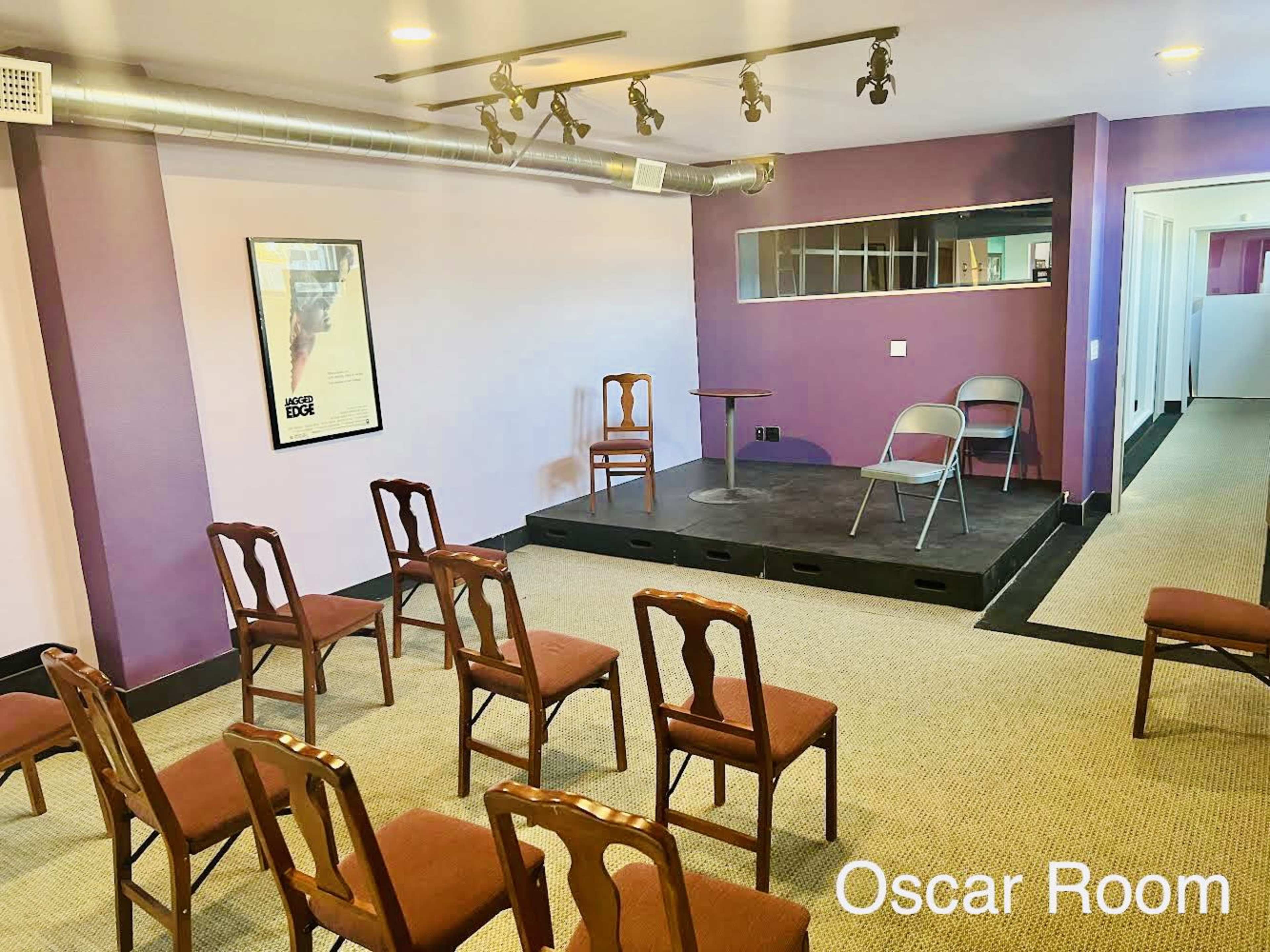 A performance space with a small stage, a few chairs arranged in rows, and a framed poster on the wall.