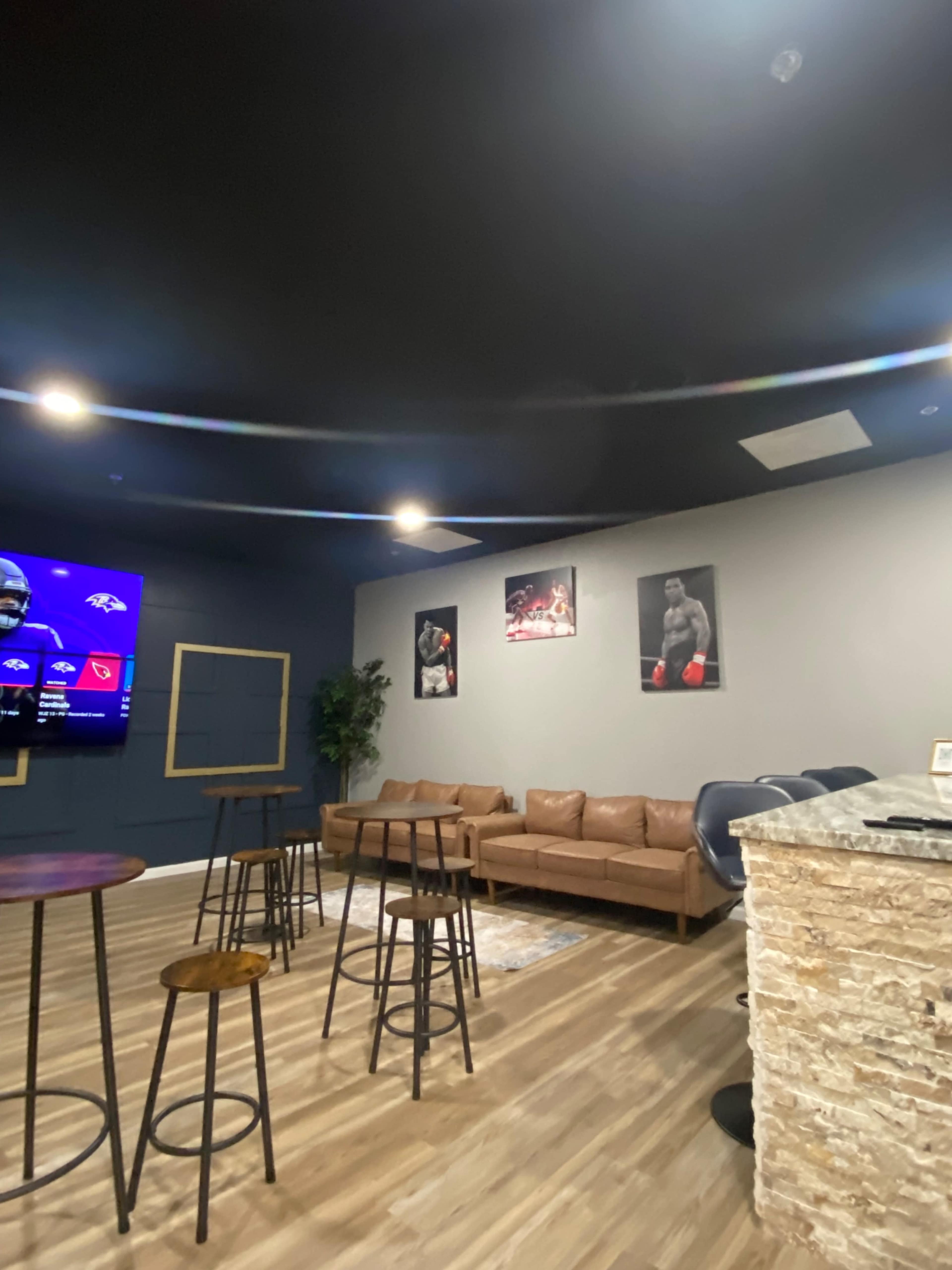 The image shows a lounge area with a bar counter, seating, and sports-themed wall art.