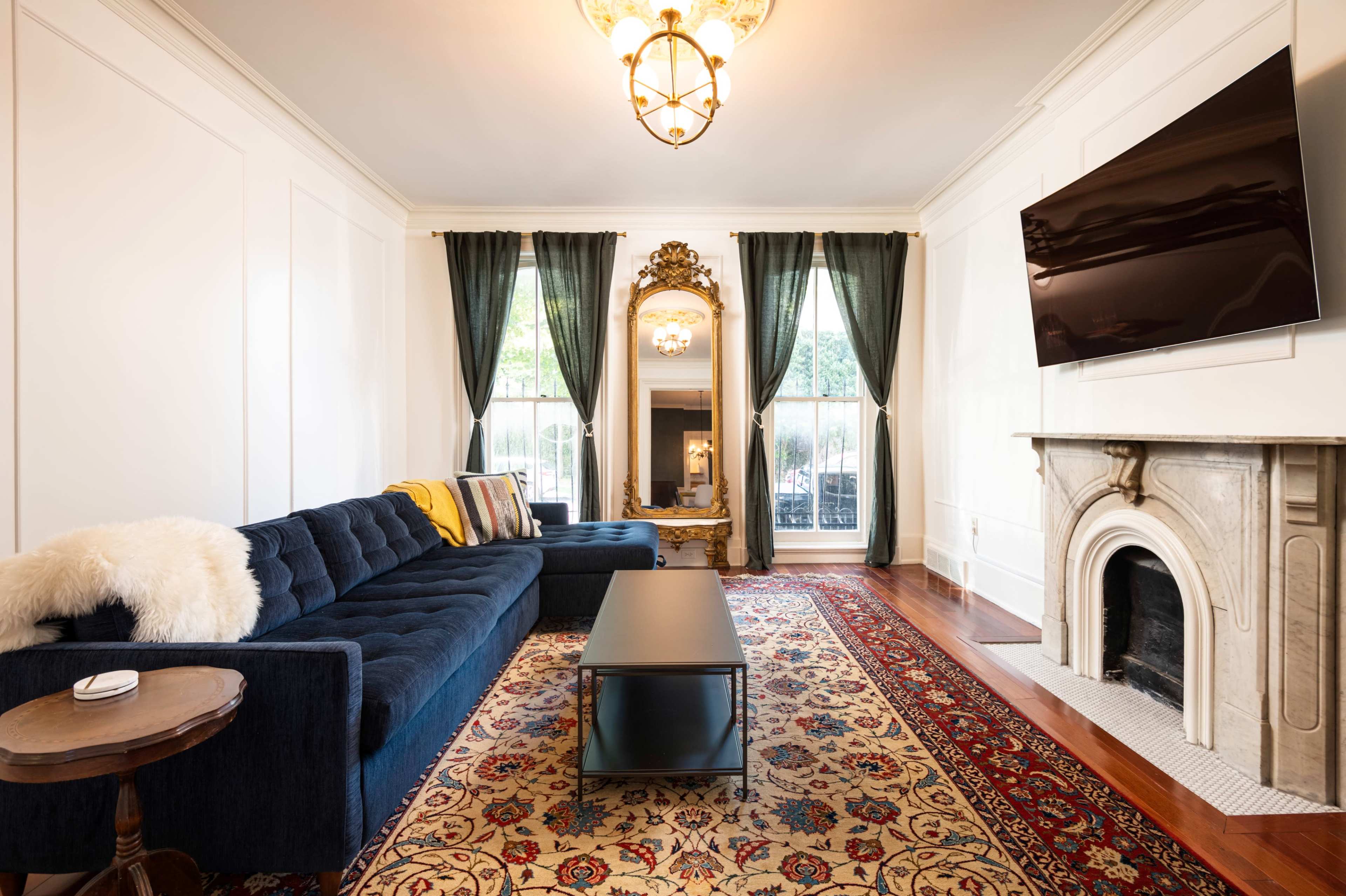 A contemporary living room featuring a blue sofa, a dark coffee table, and a decorative rug, with large windows dressed in green curtains.