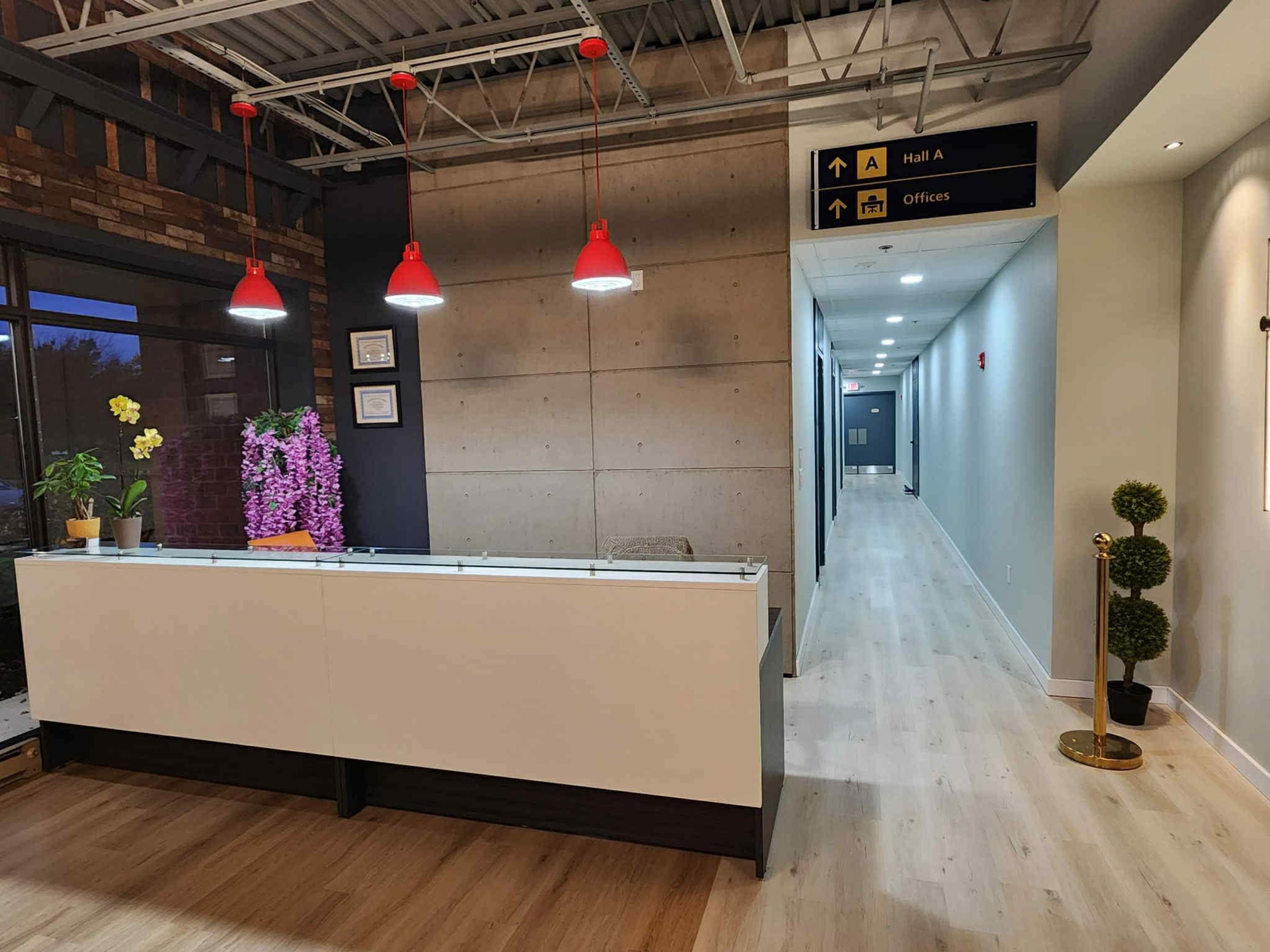 The image shows a modern reception area with a white desk, red pendant lights, and a hallway leading to additional offices.