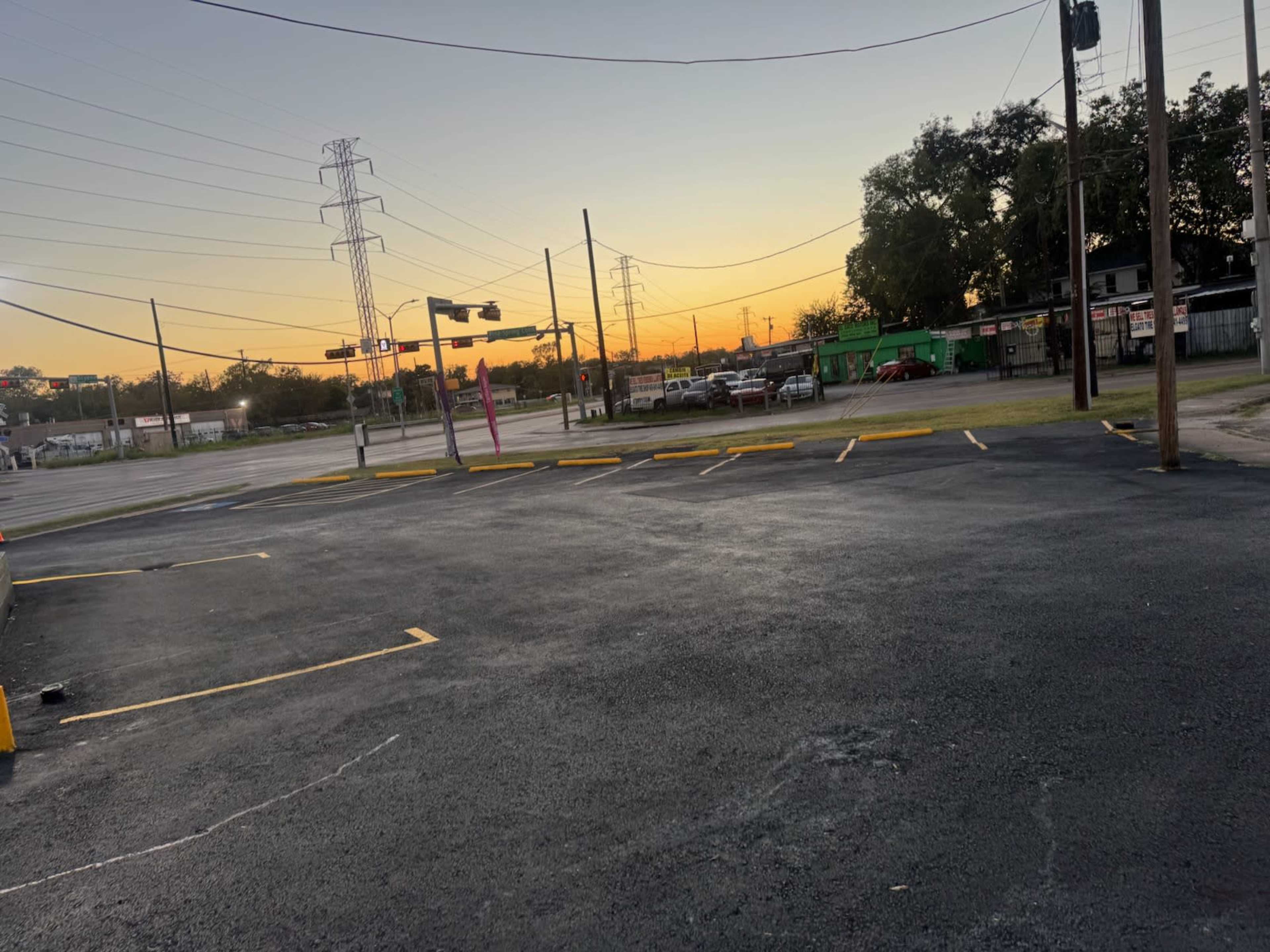The image shows an empty parking lot with painted lines, power lines above, and a sunset in the background.