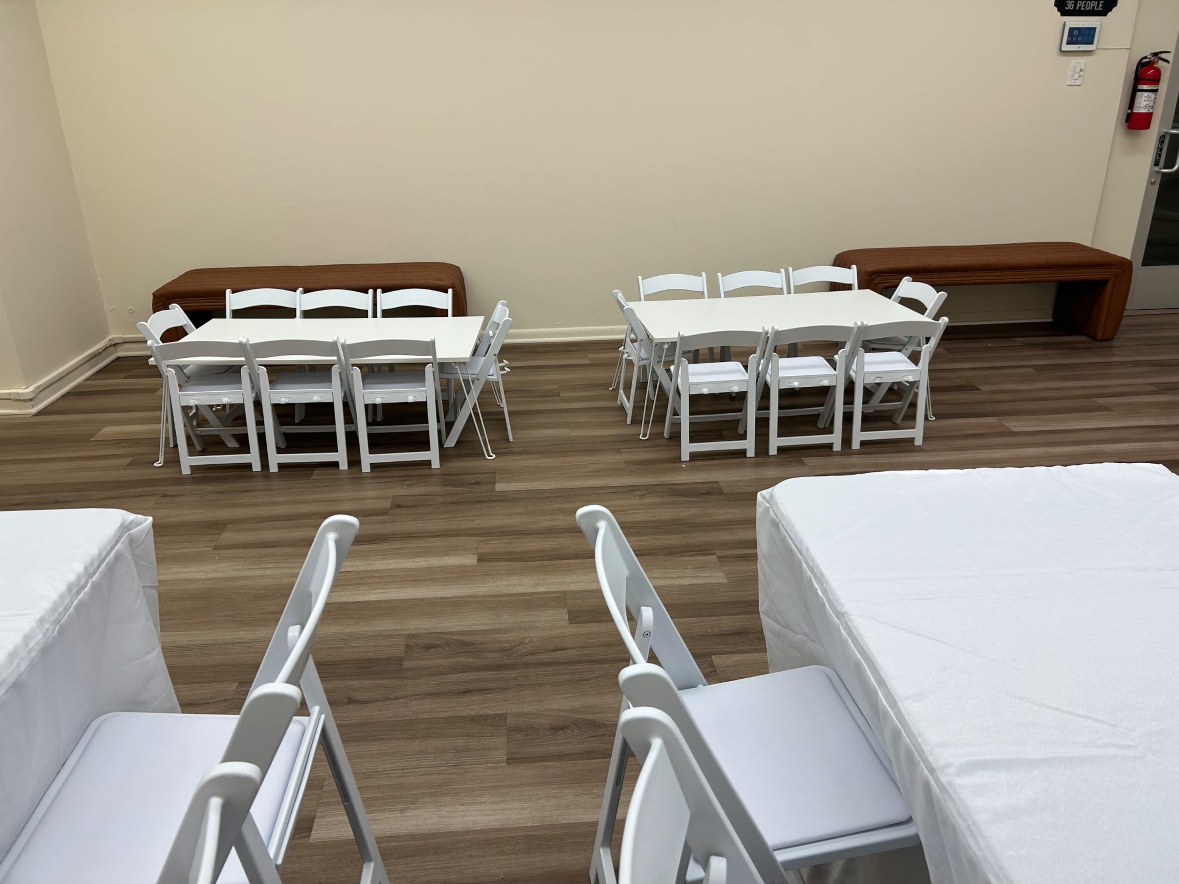 A room with several tables and chairs arranged in a simple layout, featuring two groups of tables set for a gathering or meeting.