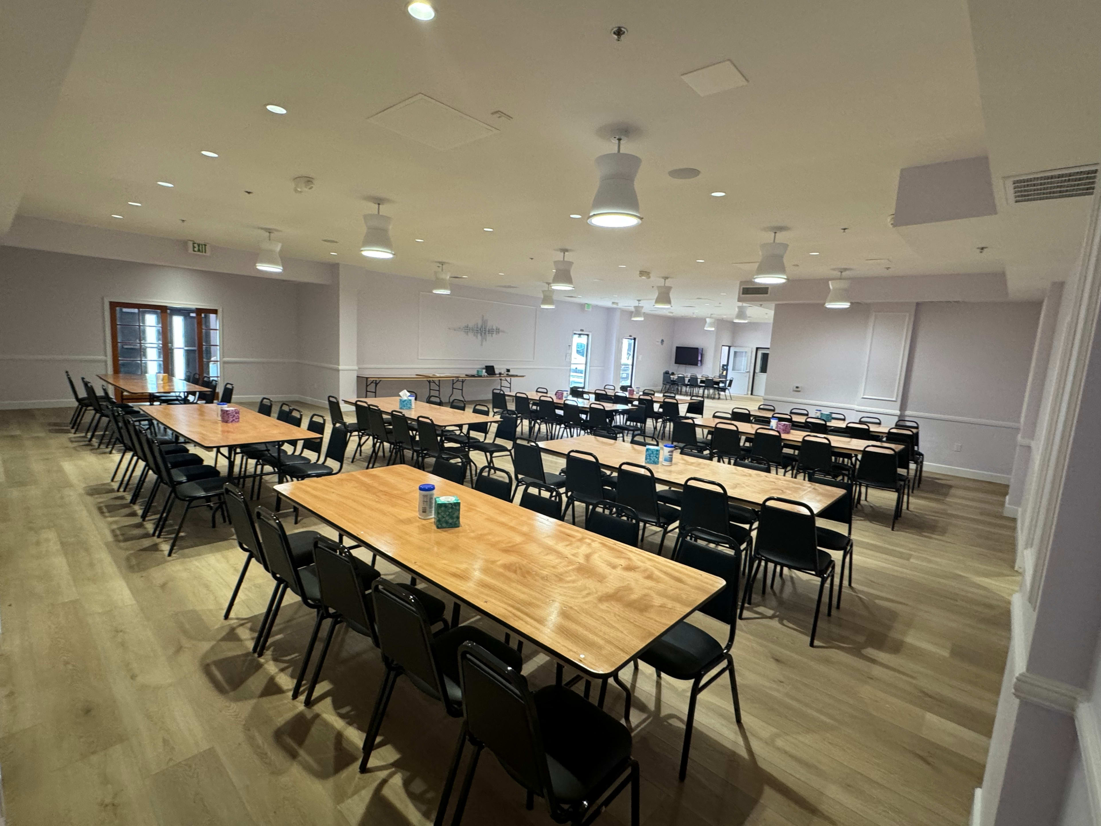 A large, empty meeting room with multiple rows of tables and chairs arranged for an event.