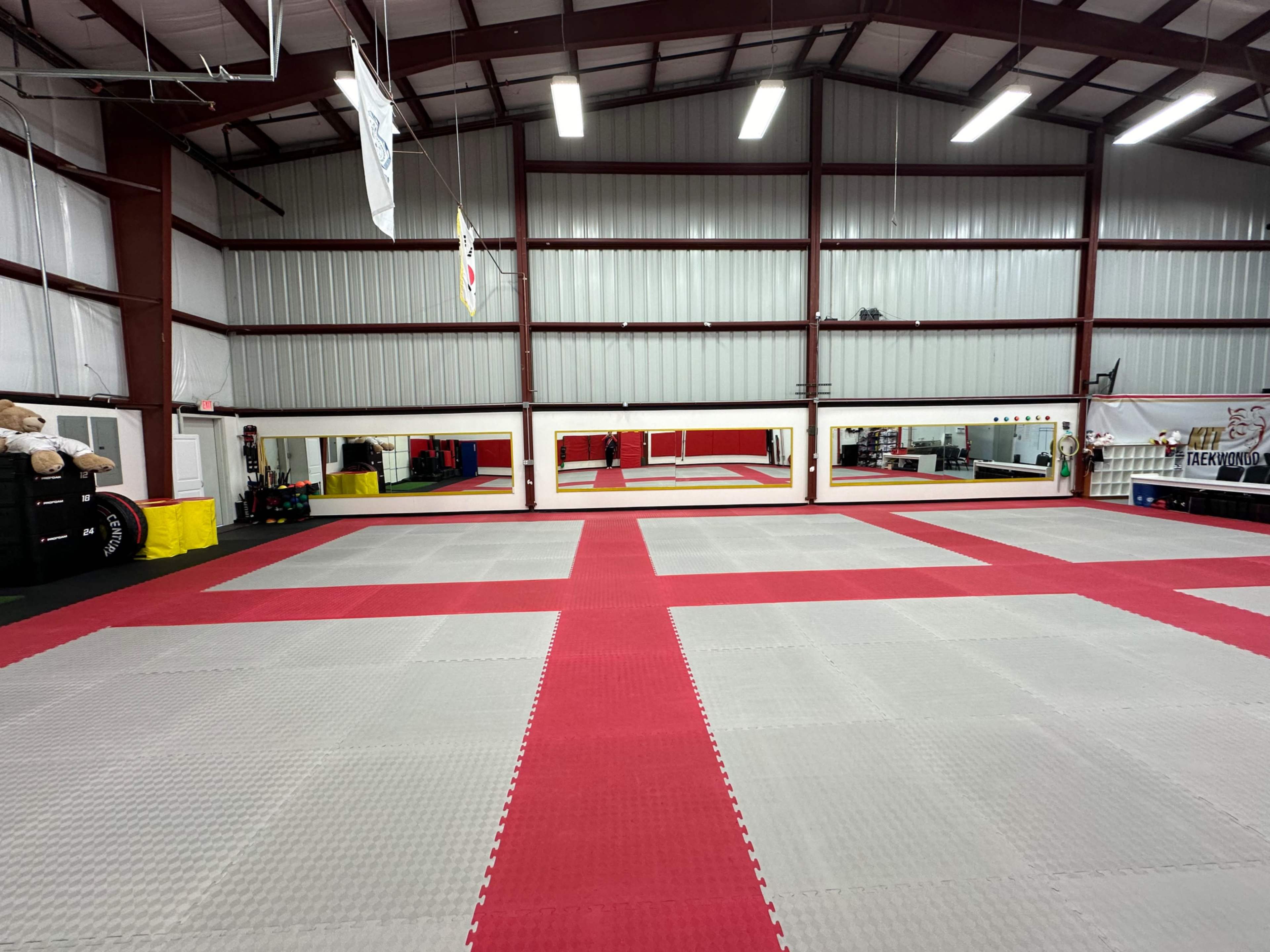 A spacious martial arts dojo with red and gray mats and large mirrors along one wall.