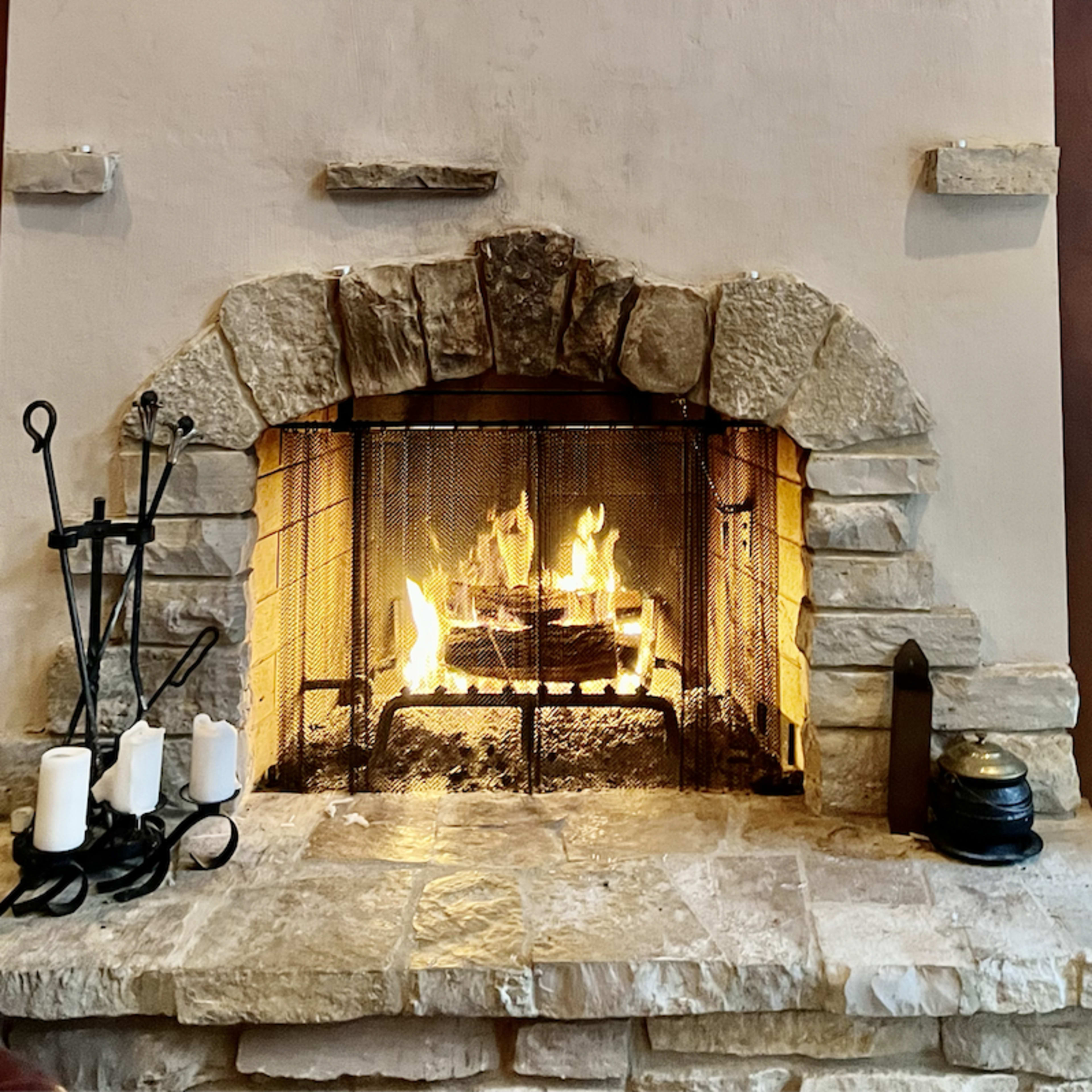 A stone fireplace with a metal screen contains a fire, surrounded by candles and a decorative lantern.