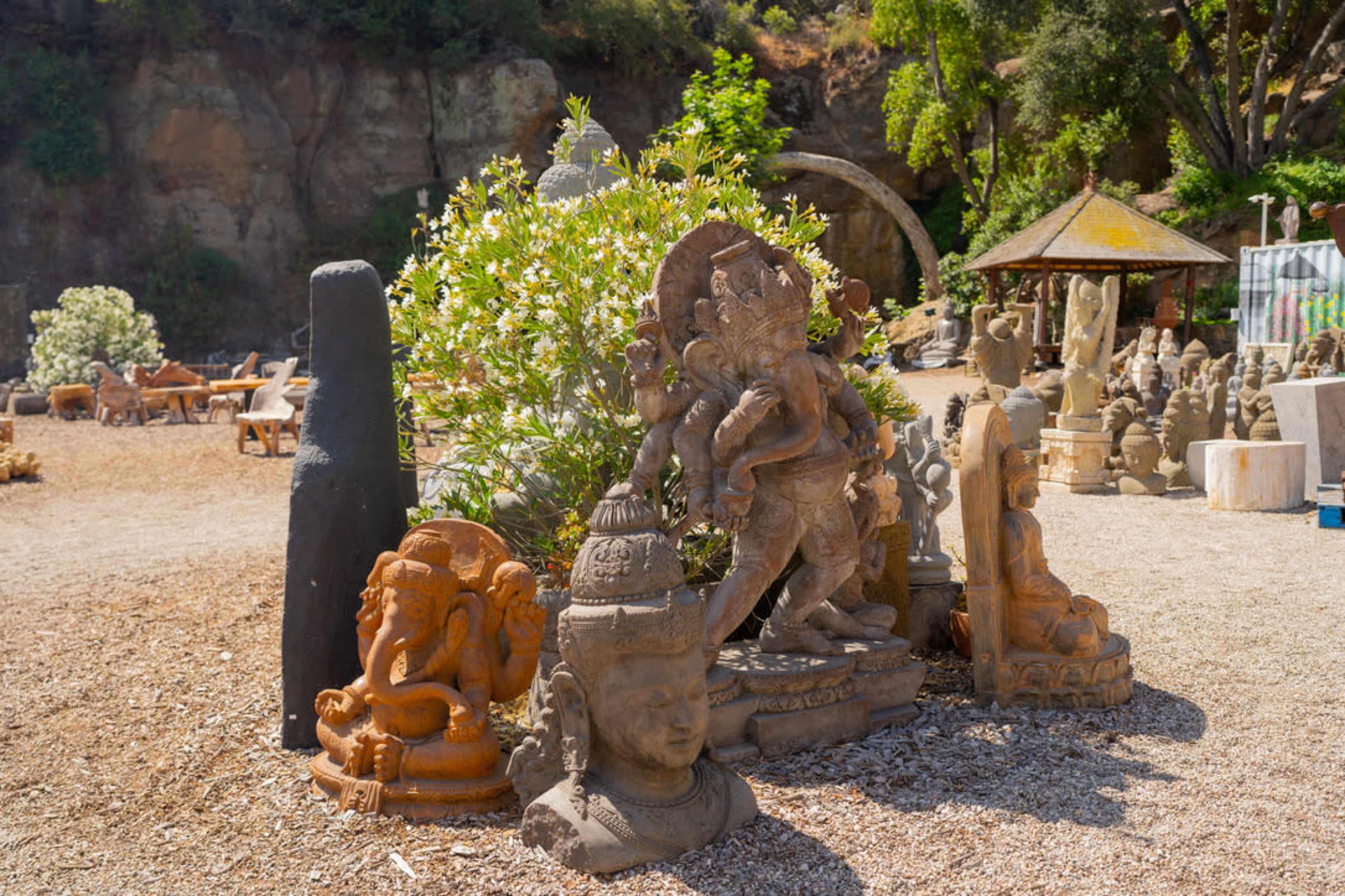 The scene features a collection of statues, including a prominent figure of Ganesh, surrounded by various stone sculptures and greenery in an outdoor setting.