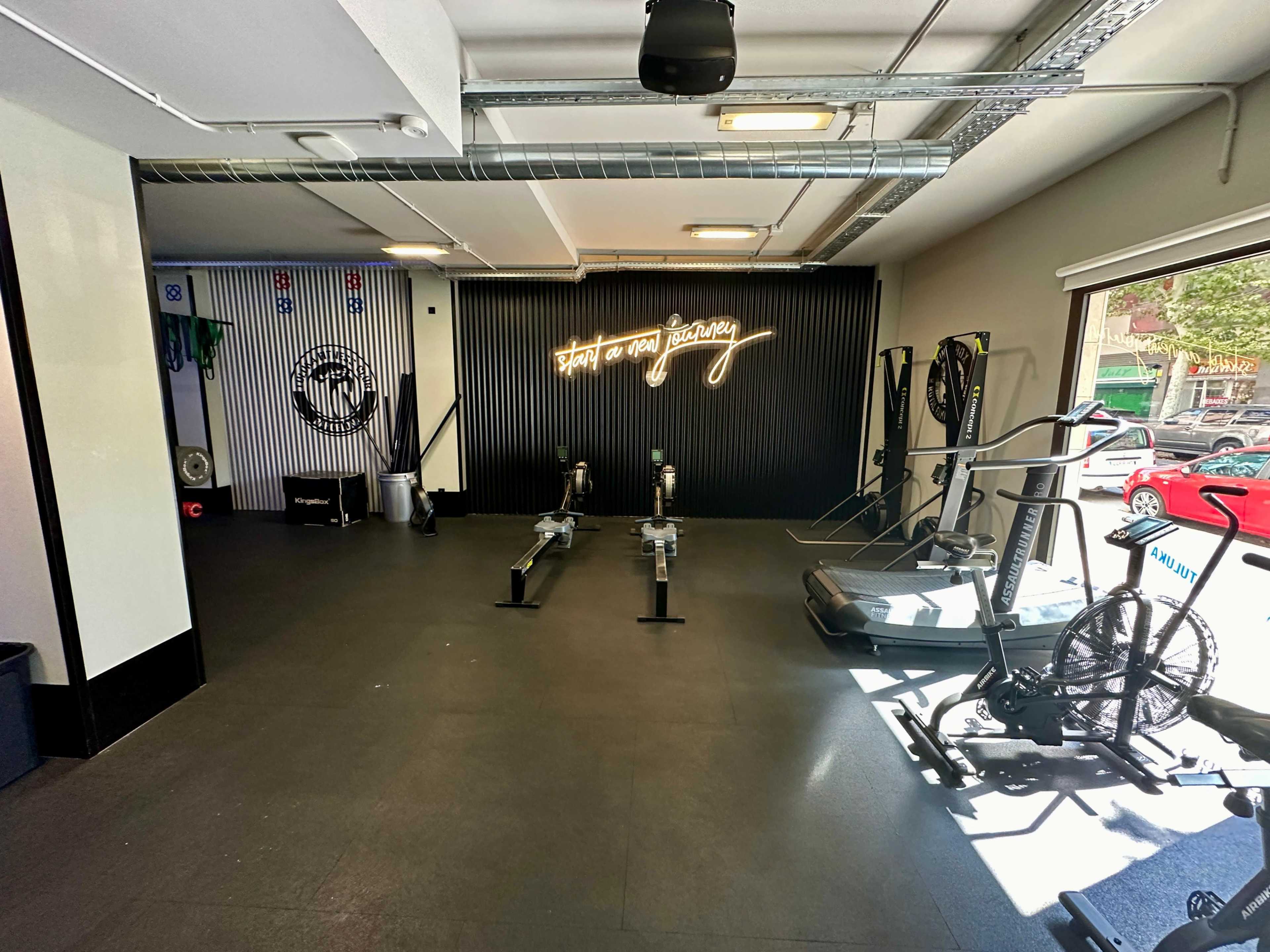 A fitness studio with exercise equipment, including rowing machines and stationary bikes, against a backdrop of a wall featuring decorative lighting.