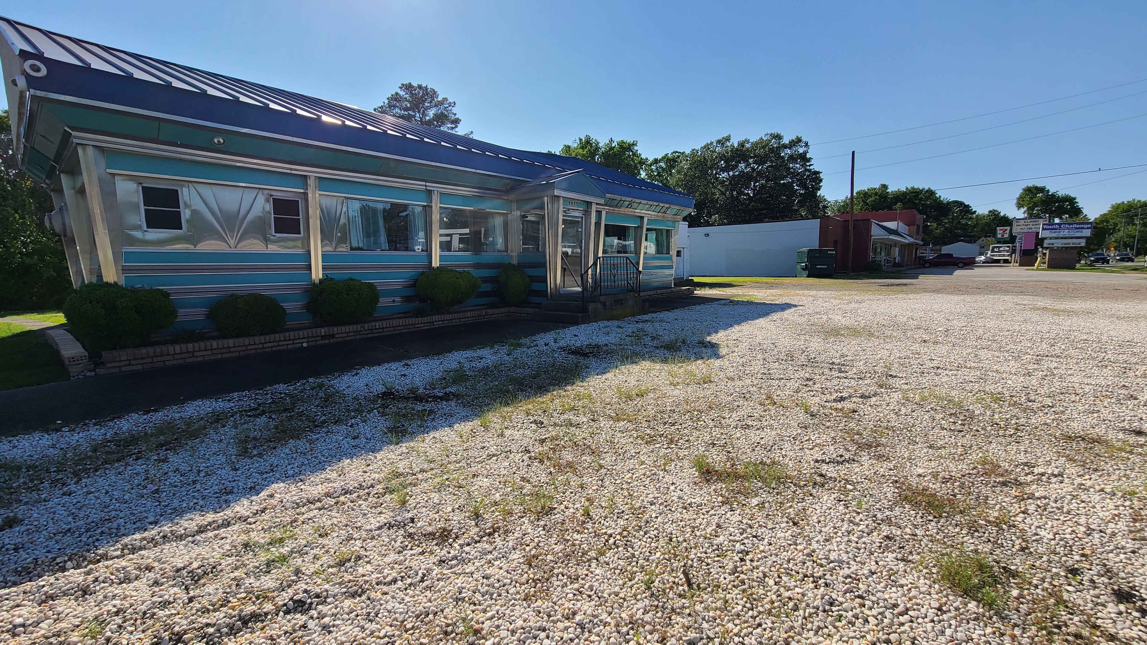 A colorful one-story building with a metal roof stands next to a gravel lot in a commercial area.