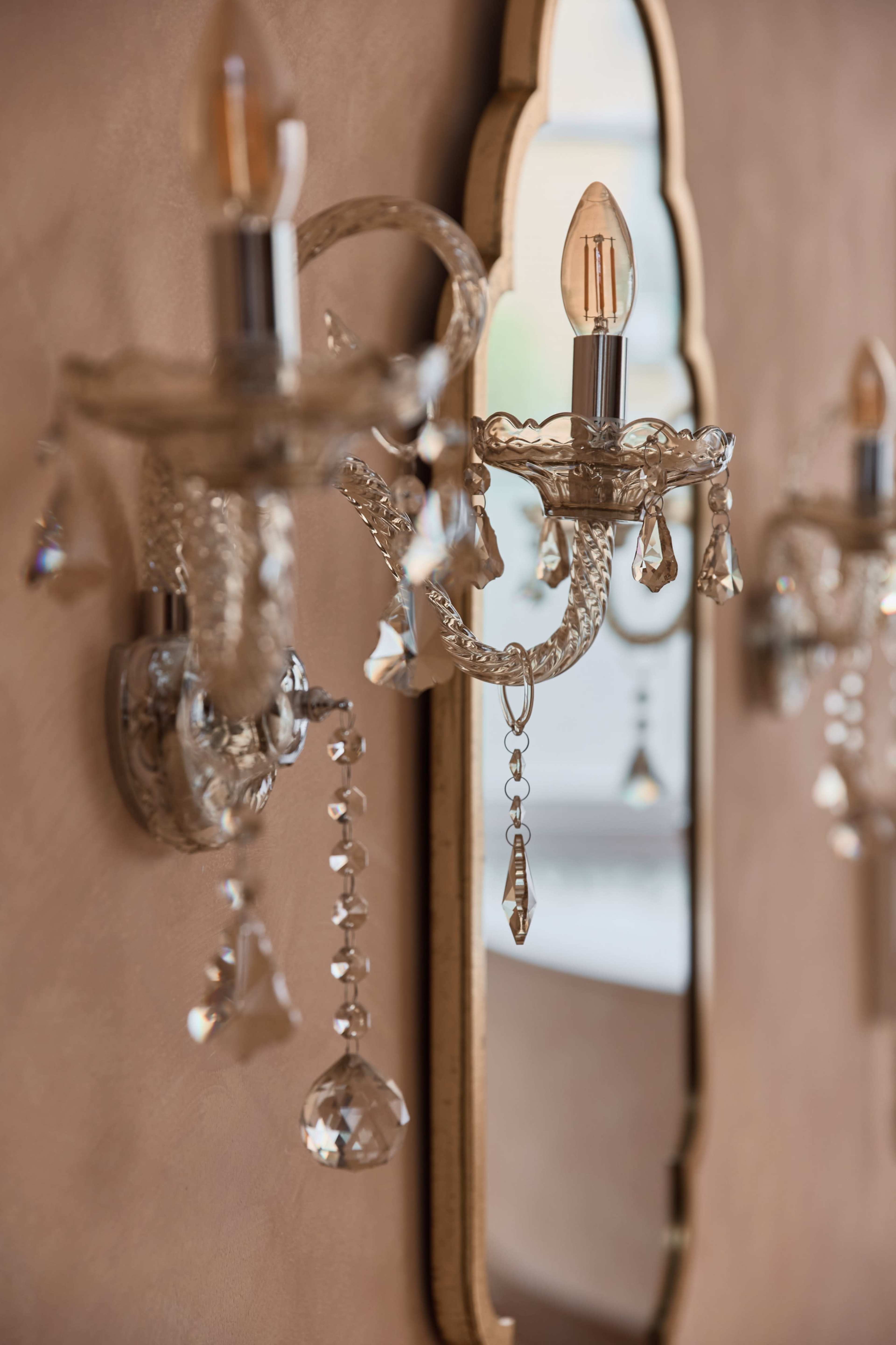 The image shows a close-up of elegant wall sconces with crystal accents beside a decorative mirror.