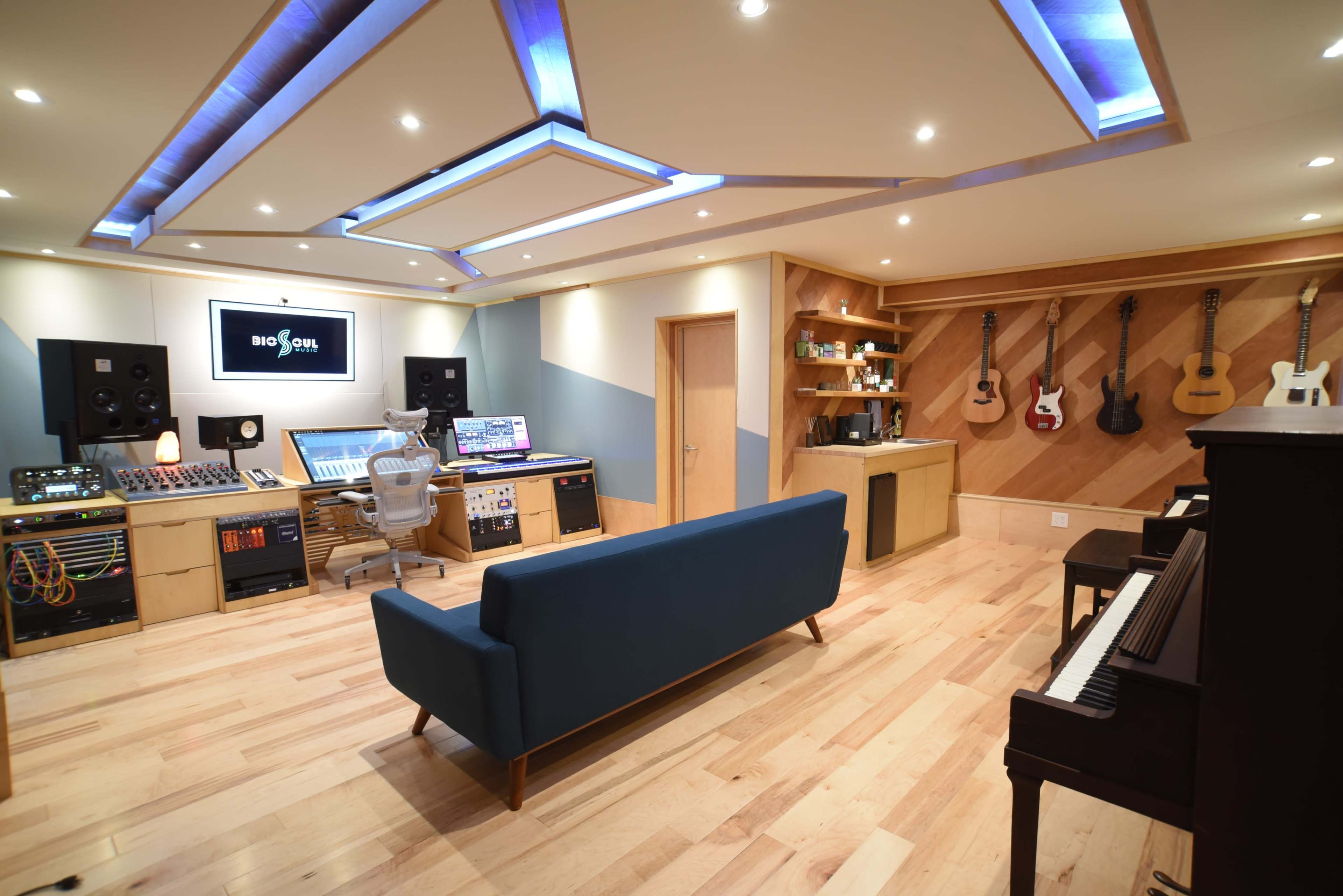 A modern music studio features a mixing console, acoustic treatment, and various musical instruments displayed on the wall.