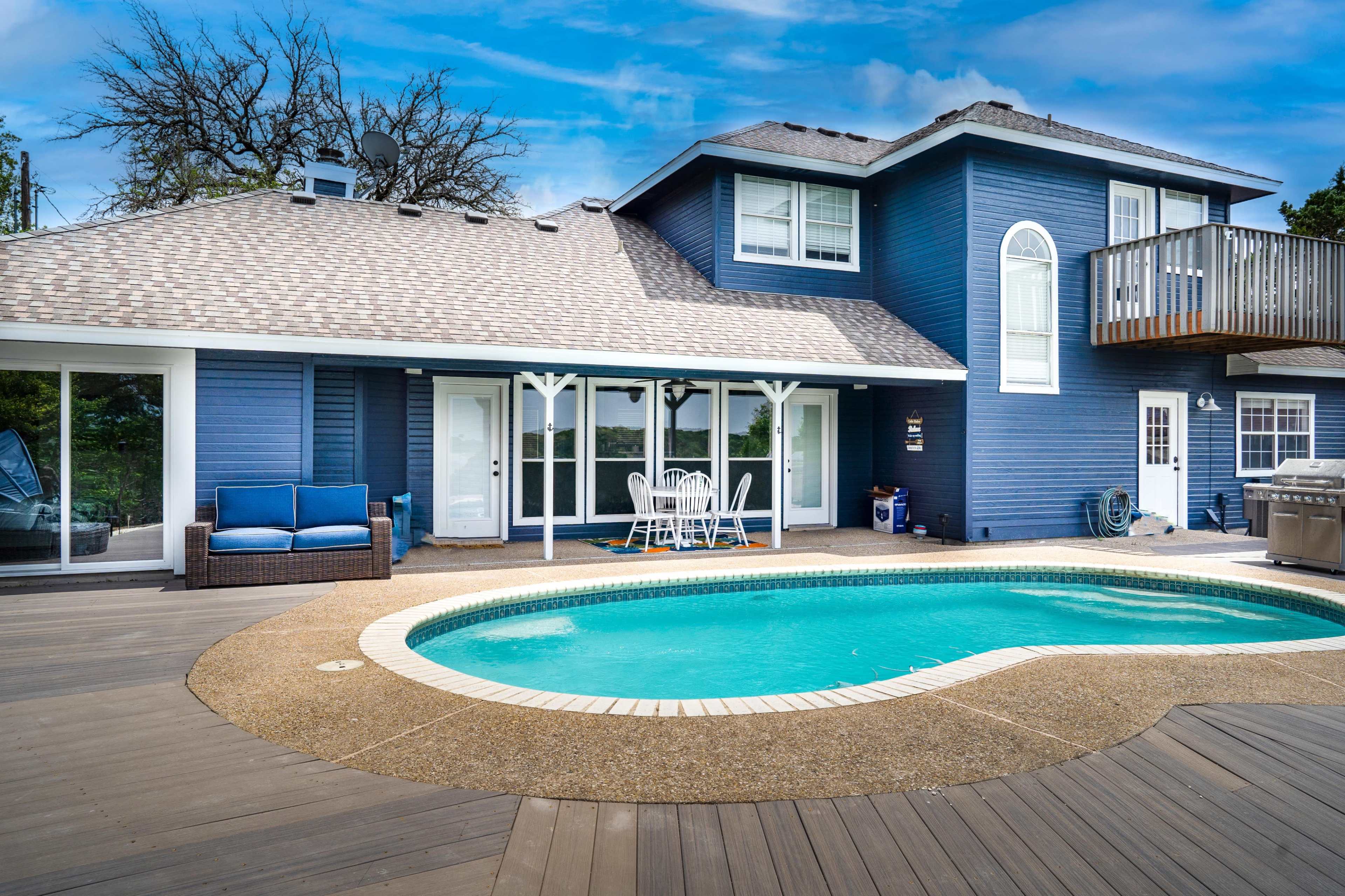 A blue two-story house with a pool and wooden deck is seen in the backyard.