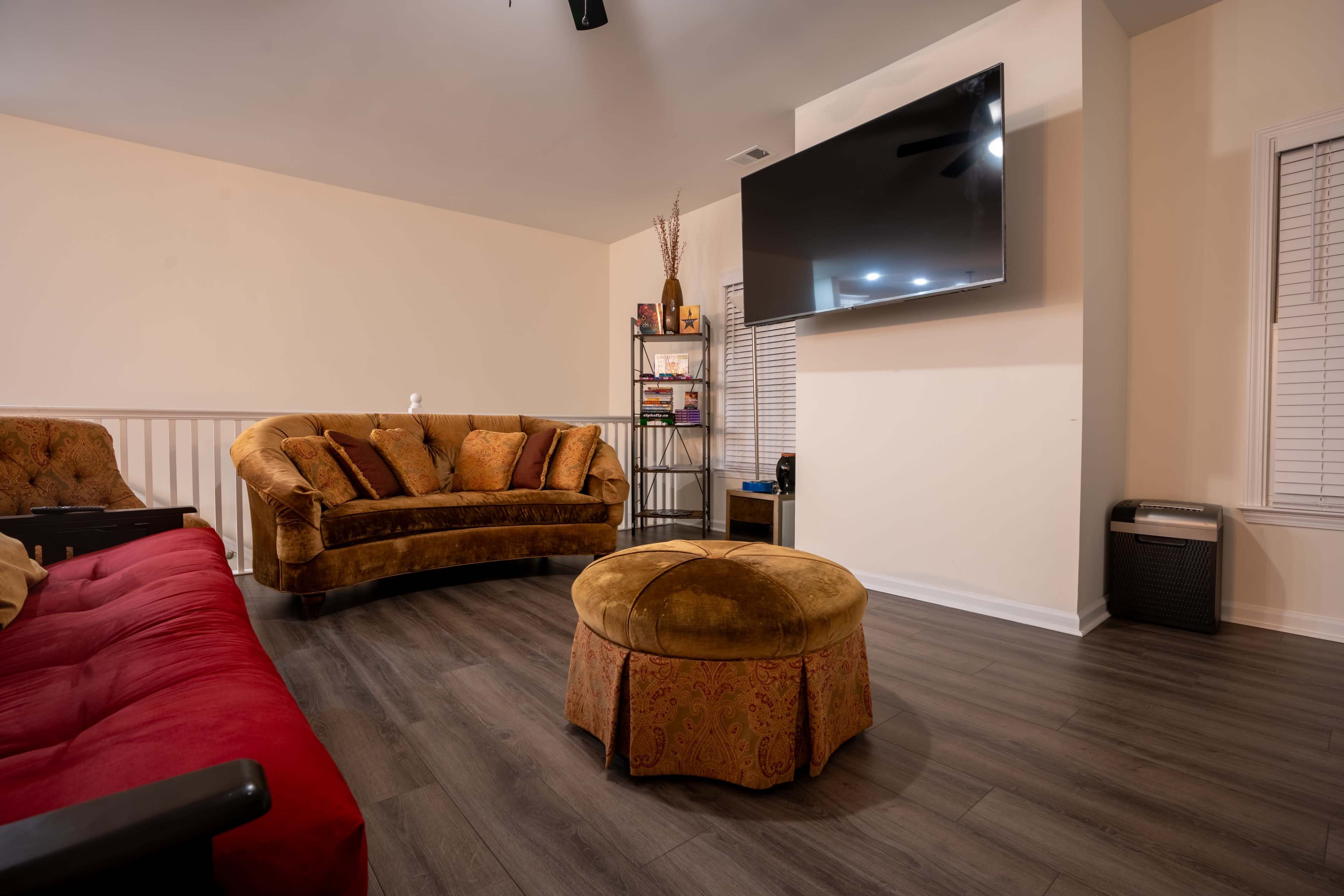 The image features a living room with two sofas, a round ottoman in the center, and a wall-mounted television.
