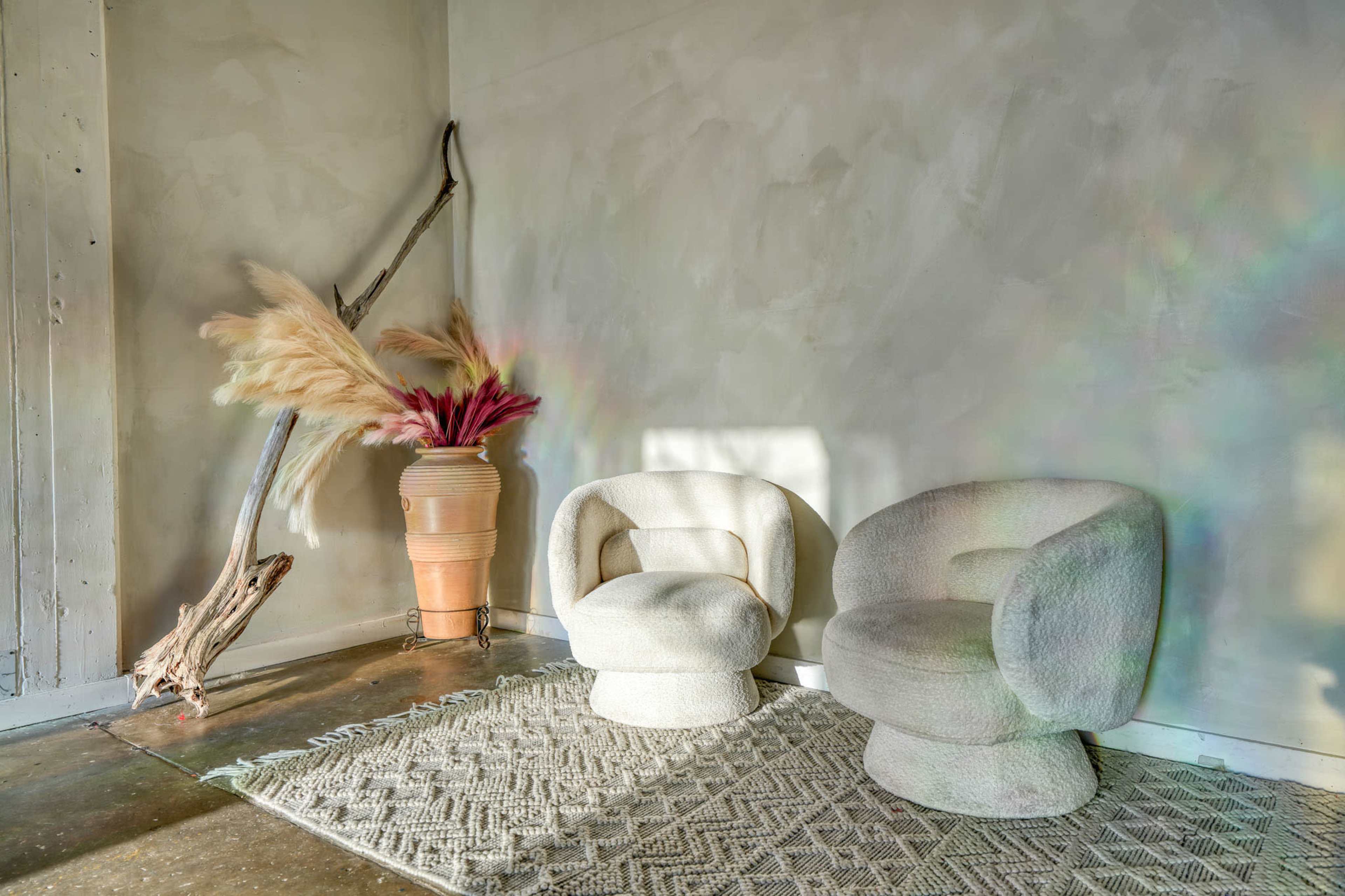 The image shows two plush, curved chairs positioned near a textured wall, accompanied by a decorative plant arrangement in a terracotta pot.