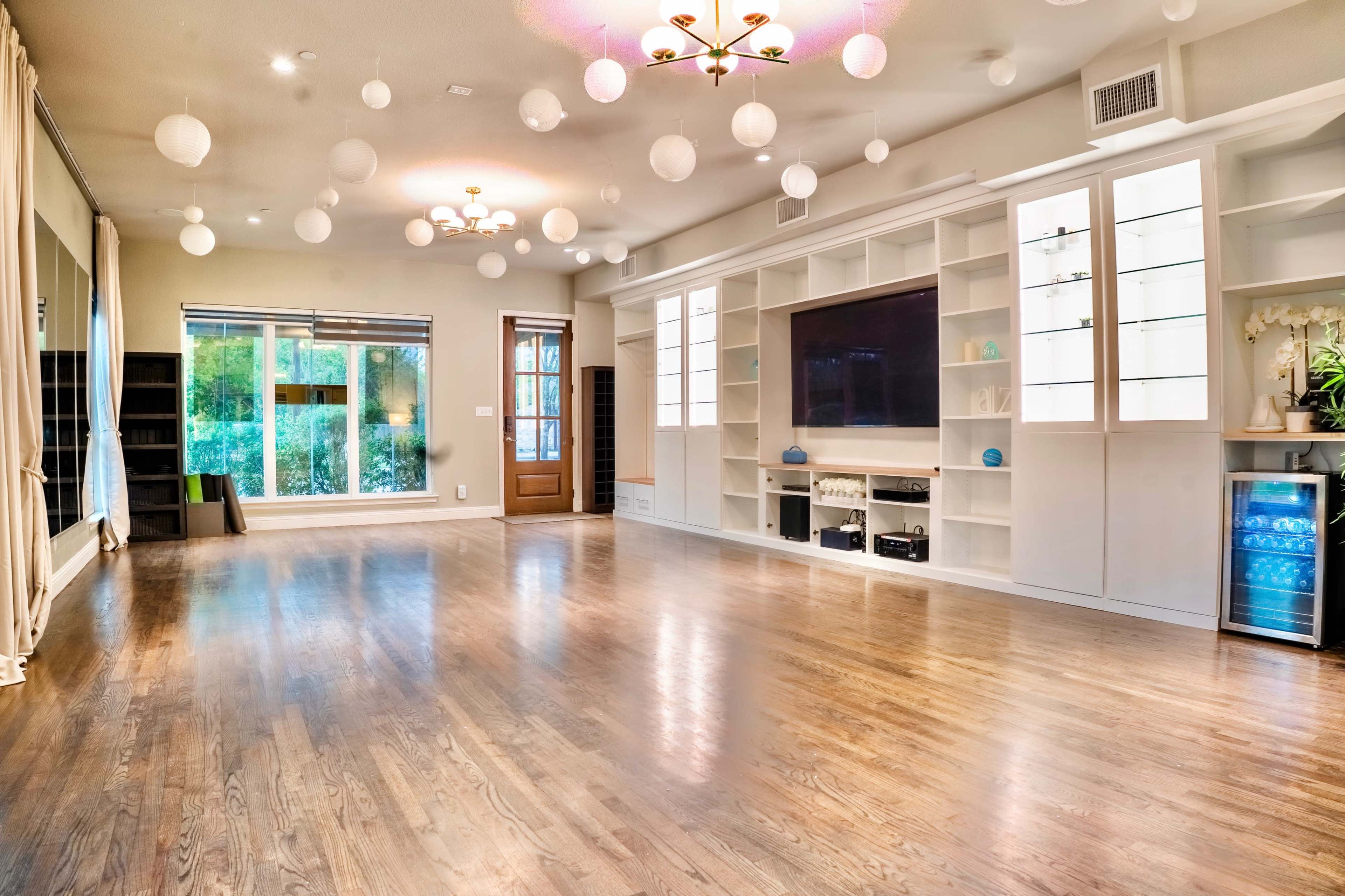 The room features hardwood floors, large windows allowing natural light, and a modern entertainment unit with built-in shelves and a mini-fridge.