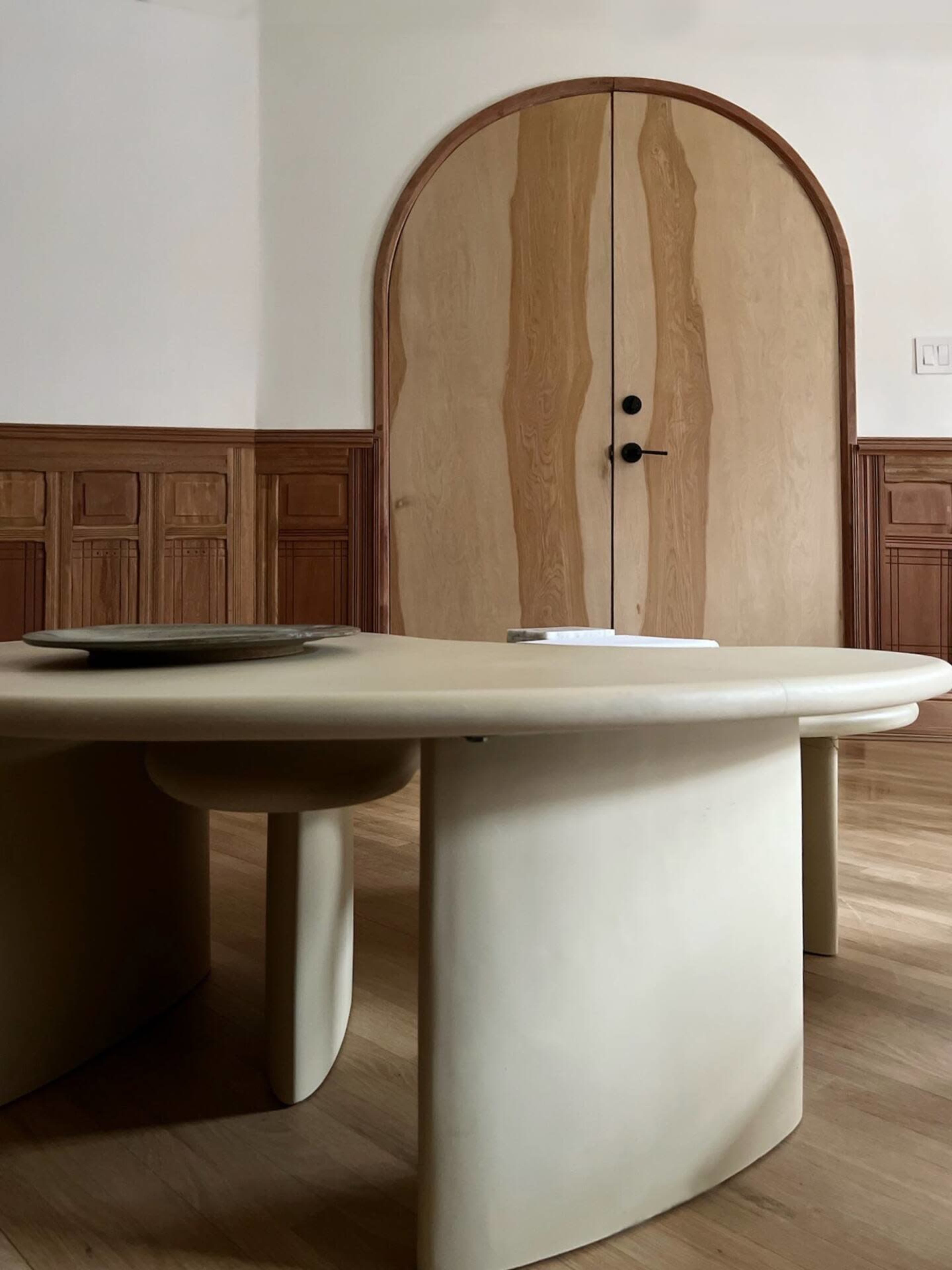 A round, low tabletop sits in the foreground with a wooden door featuring a curved top in the background.