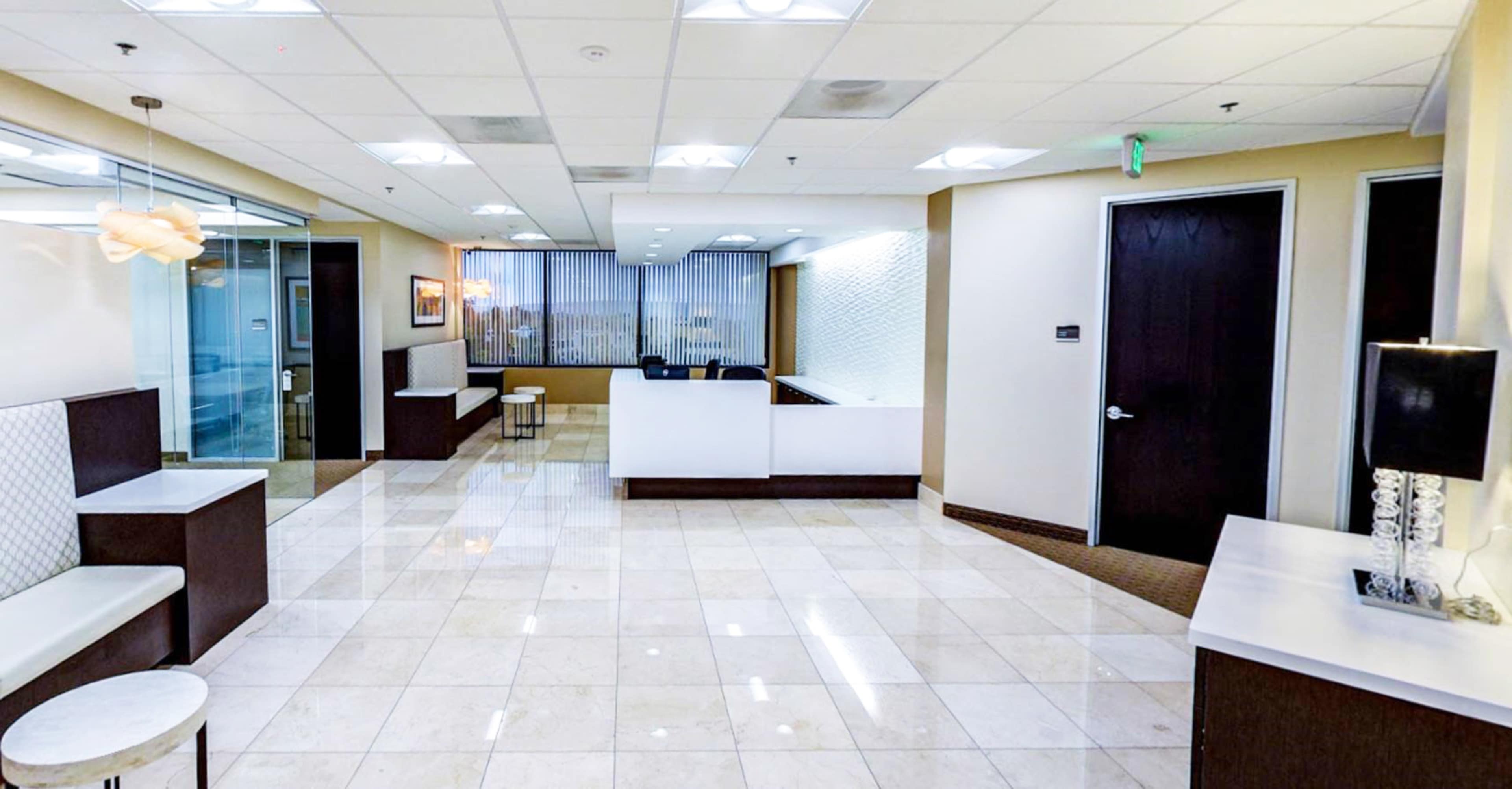 A modern office reception area with tiled flooring, beige walls, and a front desk along with seating arrangements.