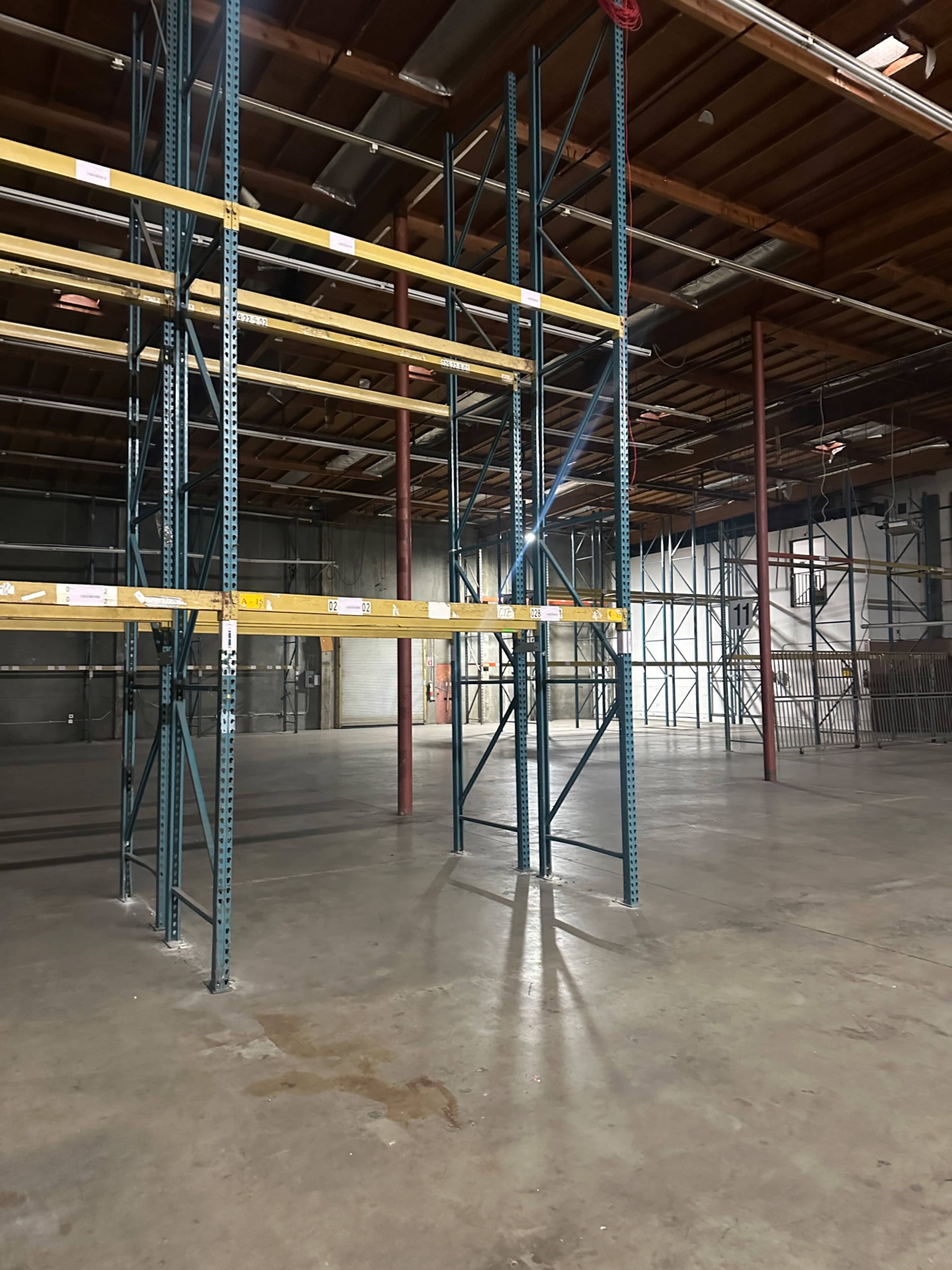 The image shows a spacious warehouse interior with metal shelving units and a concrete floor.