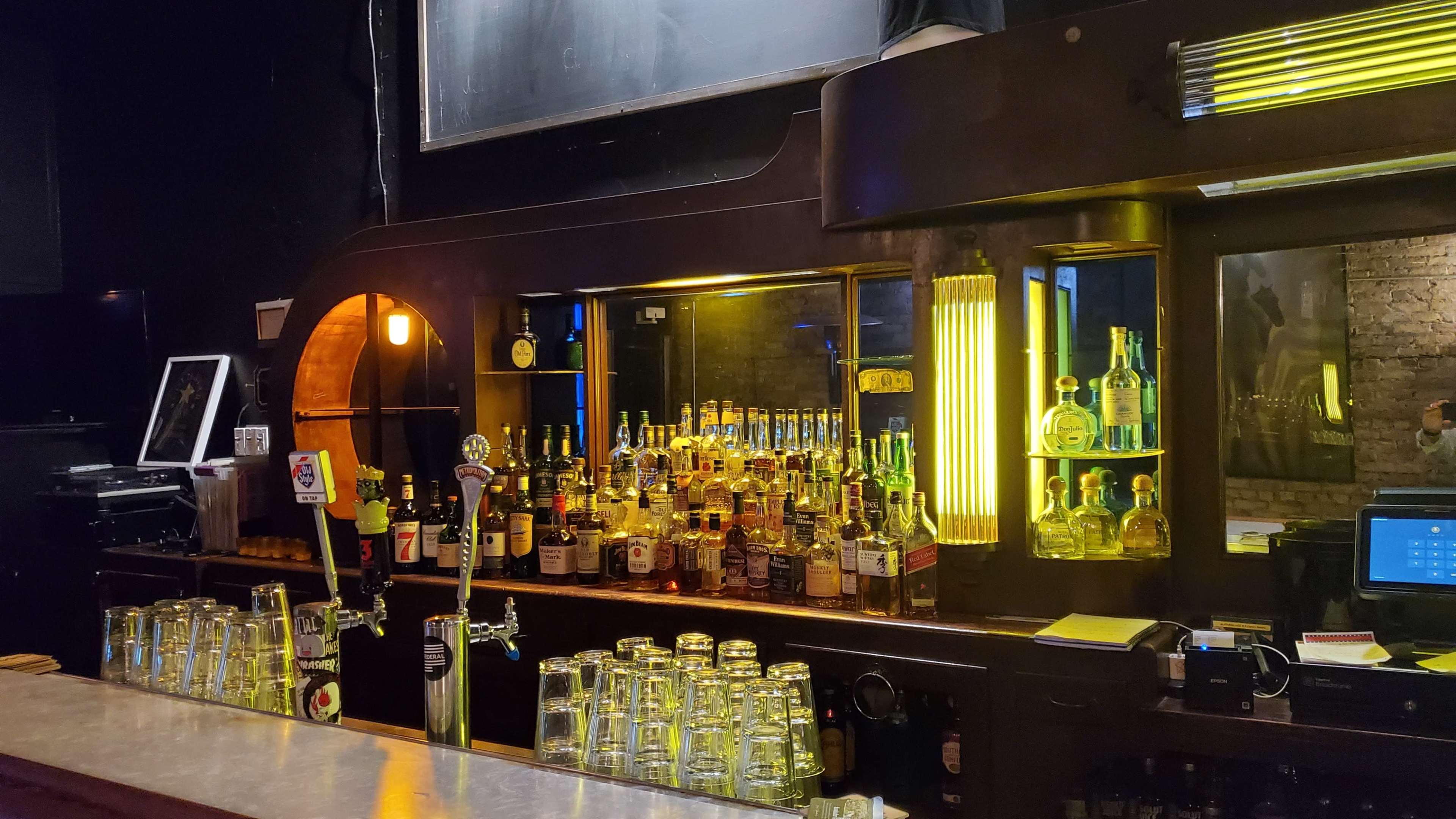 A dimly lit bar with shelves filled with various bottles of liquor and illuminated displays behind the counter.