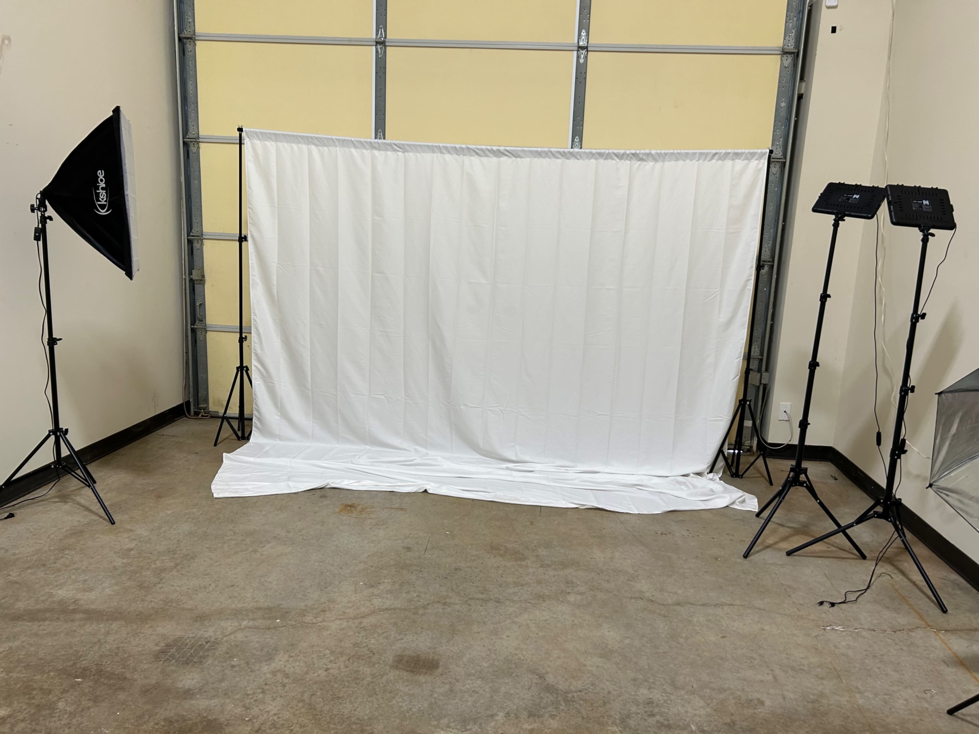 The image shows a plain white backdrop set up in a spacious room with two softbox lights positioned on either side.