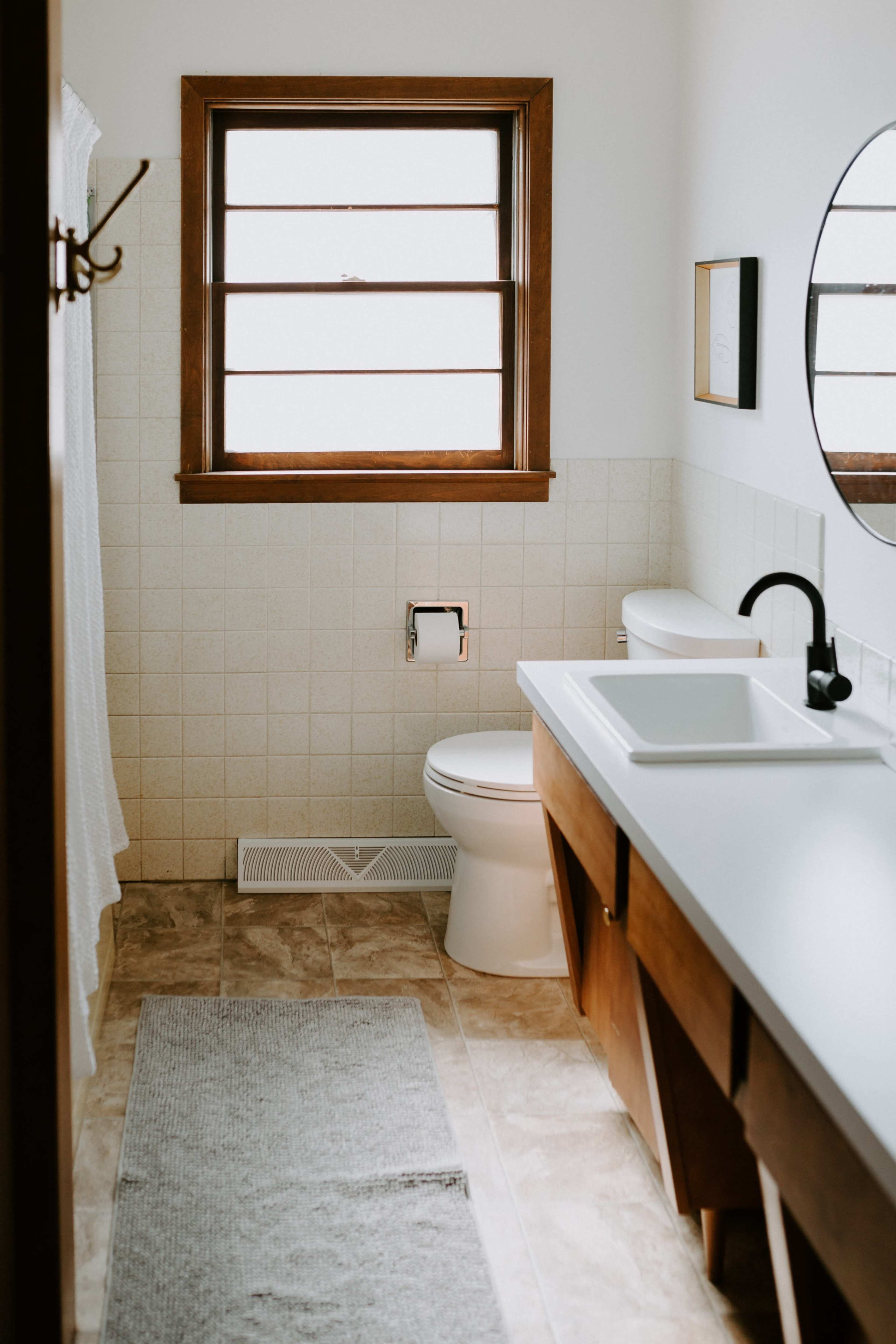 A bathroom features a toilet, a sink with a countertop, and a window with wooden trim.